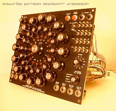 Thomas White's rotary sequencer, photographed at an angle under warm light. A tall black front panel is covered in knobs arranged in concentric circles around a central knob, with a column of switches and jacks down the right side and a row of jacks along the bottom. The words "music from outer space" run across the top of the photo.