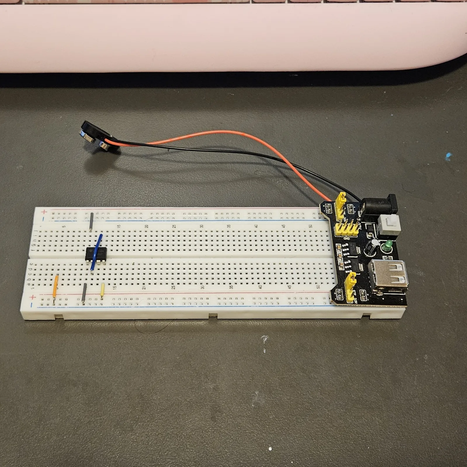 The breadboard with the chip in place and the jumper wires added. A blue jumper stands vertically beside the chip and short jumpers run from the rows either side of it down into the rails. The power module and its 9-volt battery sit at the right-hand end, and the rest of the board is still empty.