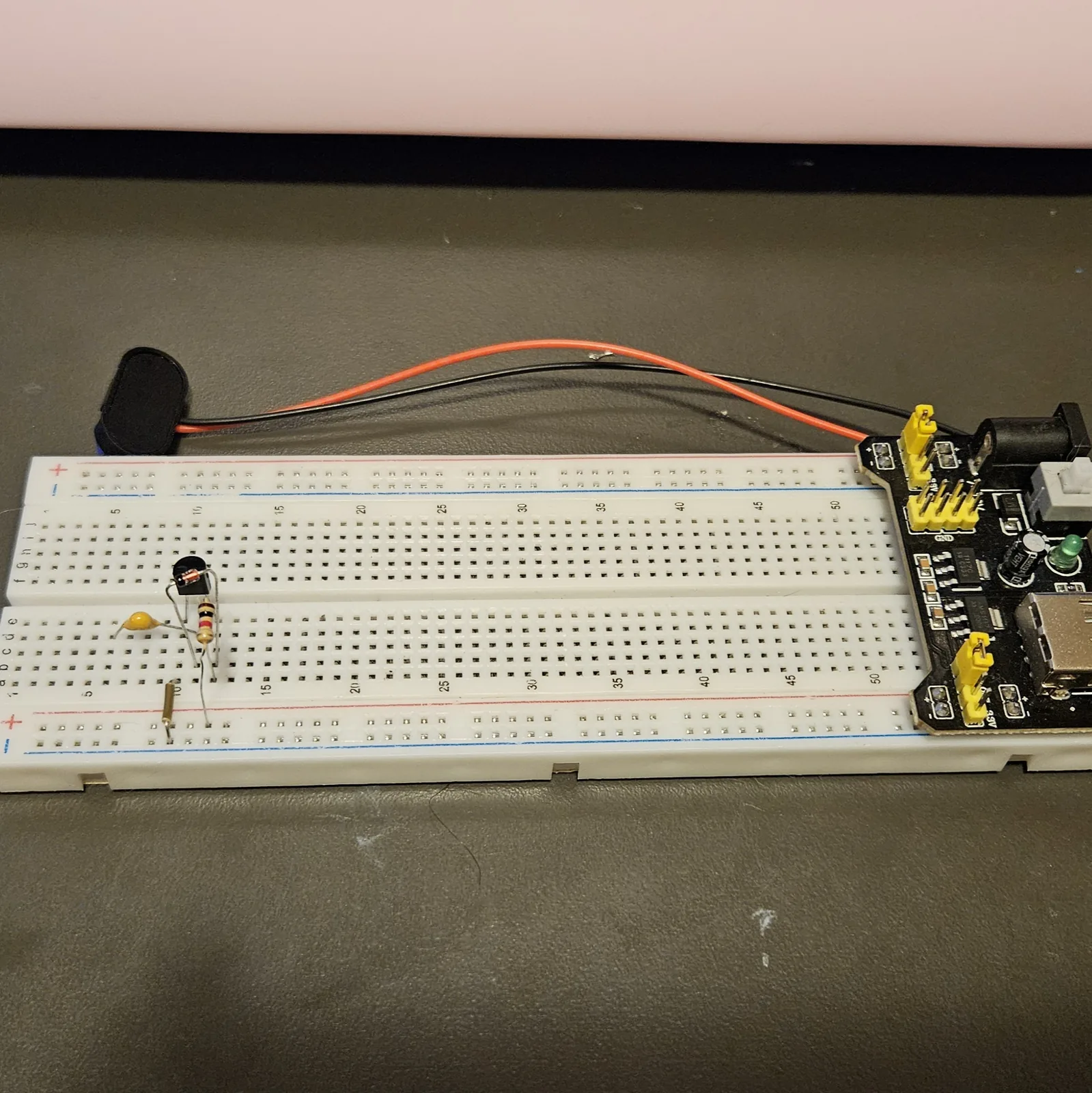 A small yellow film capacitor added upright on the board to the left of the transistor, its two legs in adjacent rows, with the rest of the circuit behind it.