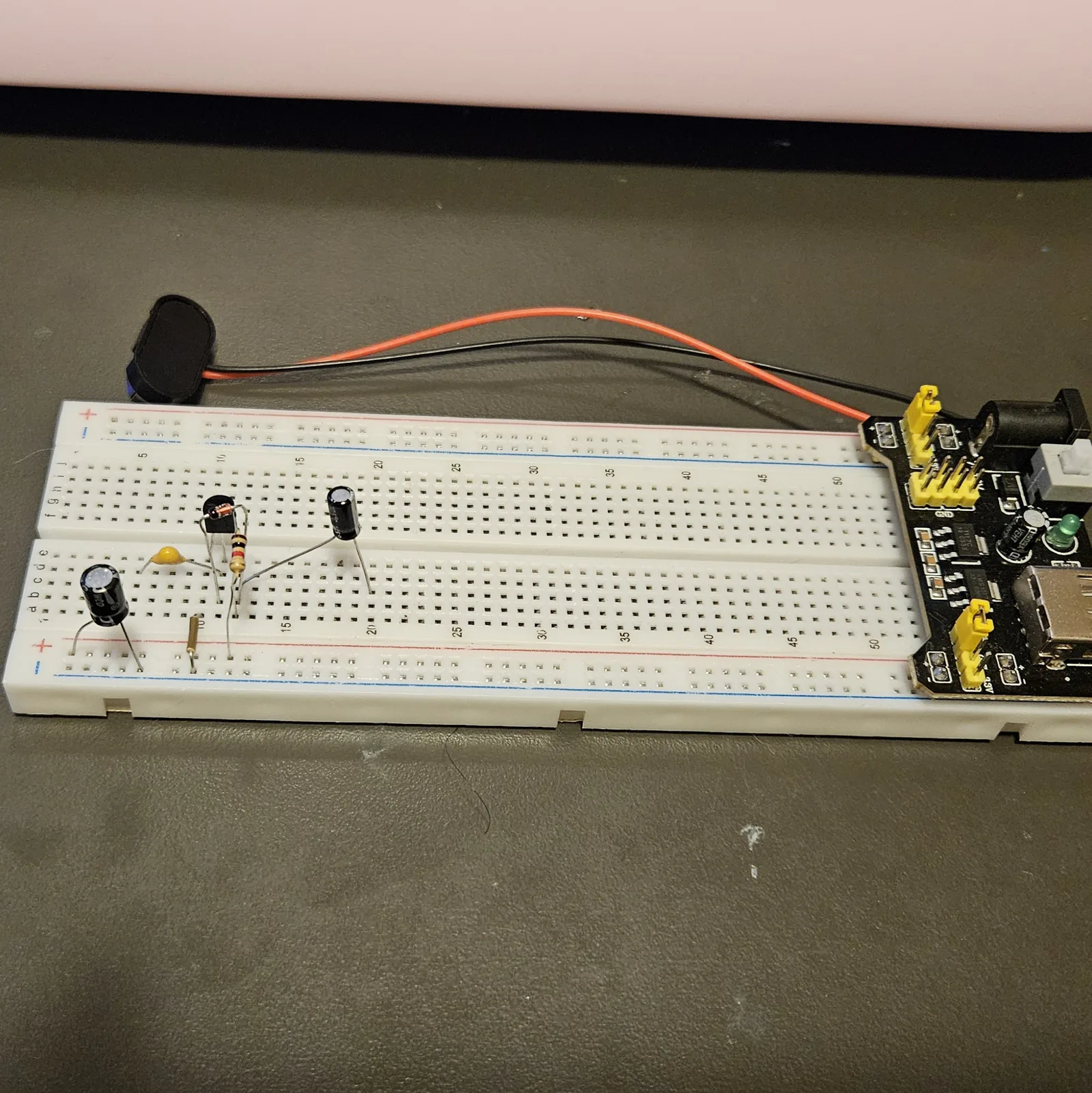 A black electrolytic capacitor can added at the left of the board with its legs in the two supply rails, standing beside the yellow film capacitor and the transistor.