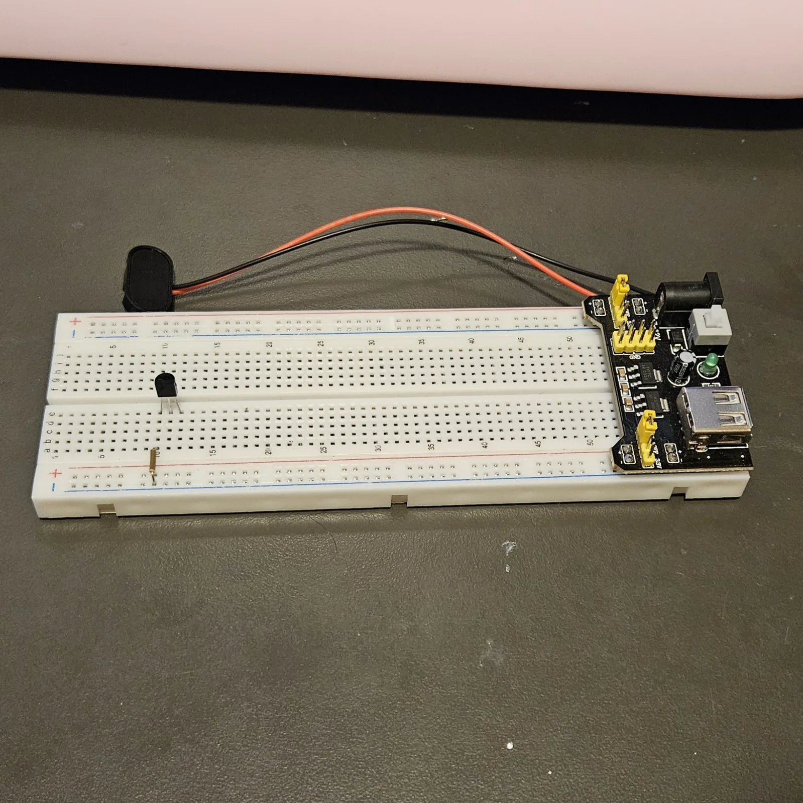 The same board with a short bare jumper added beside the transistor, linking one of its rows across to the neighbouring strip. The rest of the board is still empty.