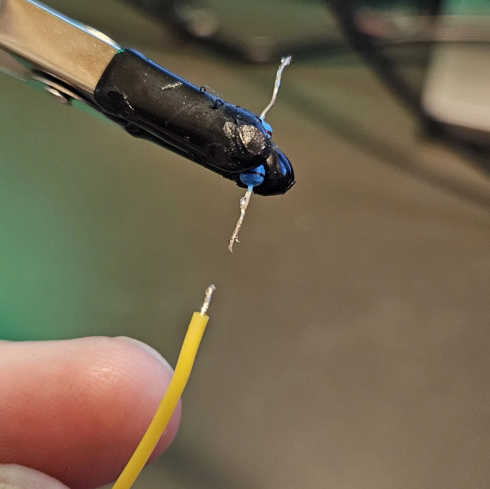 A stripped yellow hookup wire held up beside a clip, its exposed end freshly tinned so the strands are fused into one solid silver tip.