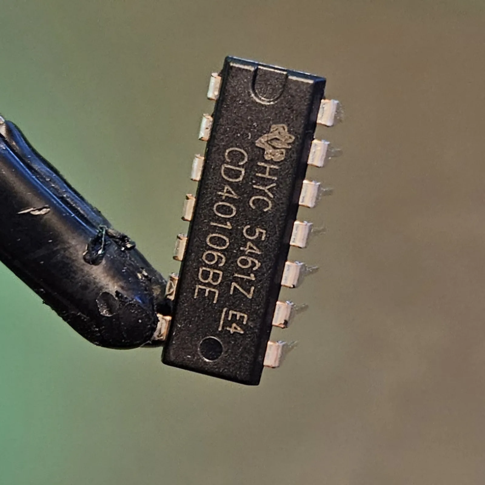 A CD40106 integrated circuit held in a clip, its black 14-pin DIP body printed CD40106 with the notch at one end marking pin 1.