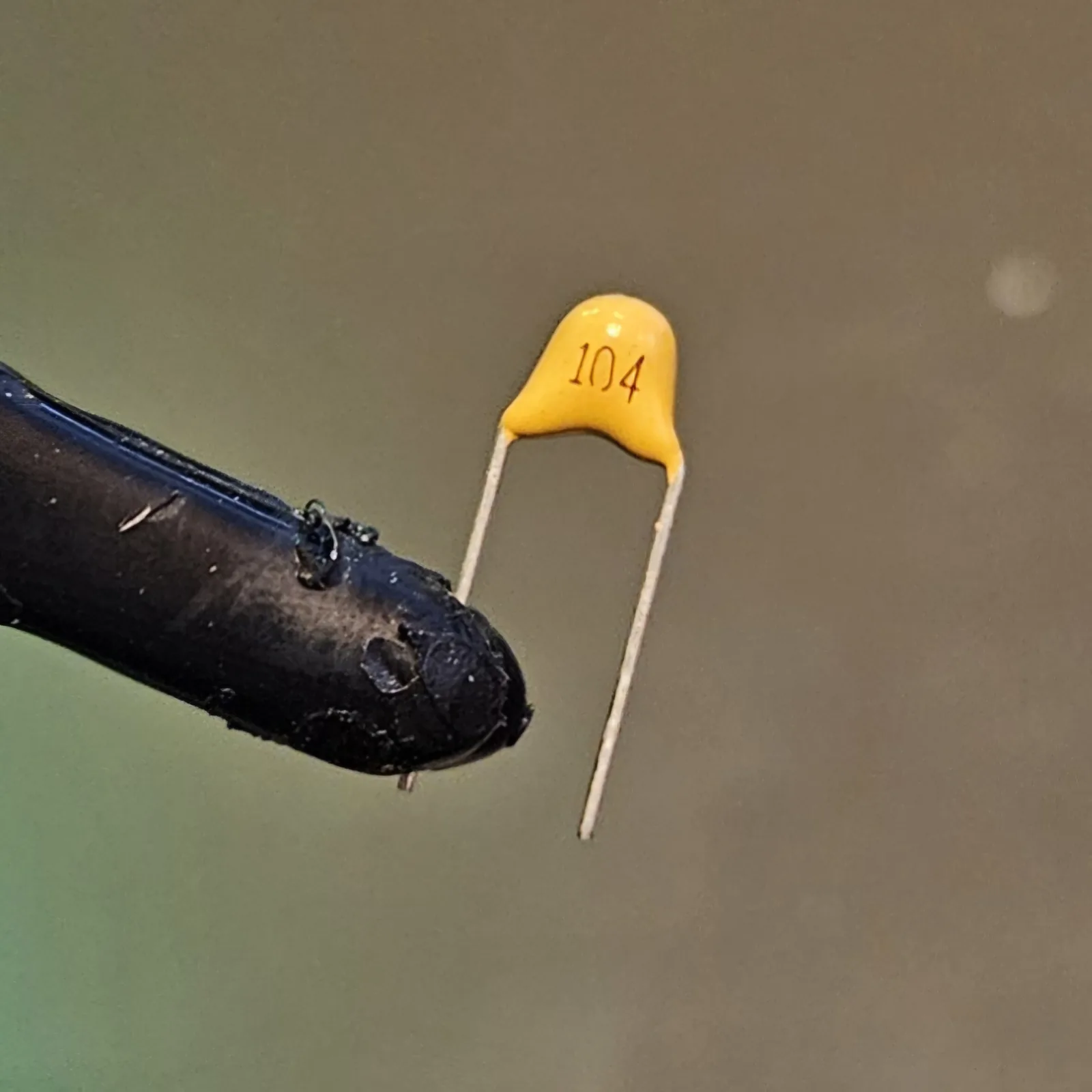 A single yellow ceramic capacitor with its two silver legs, printed 104.
