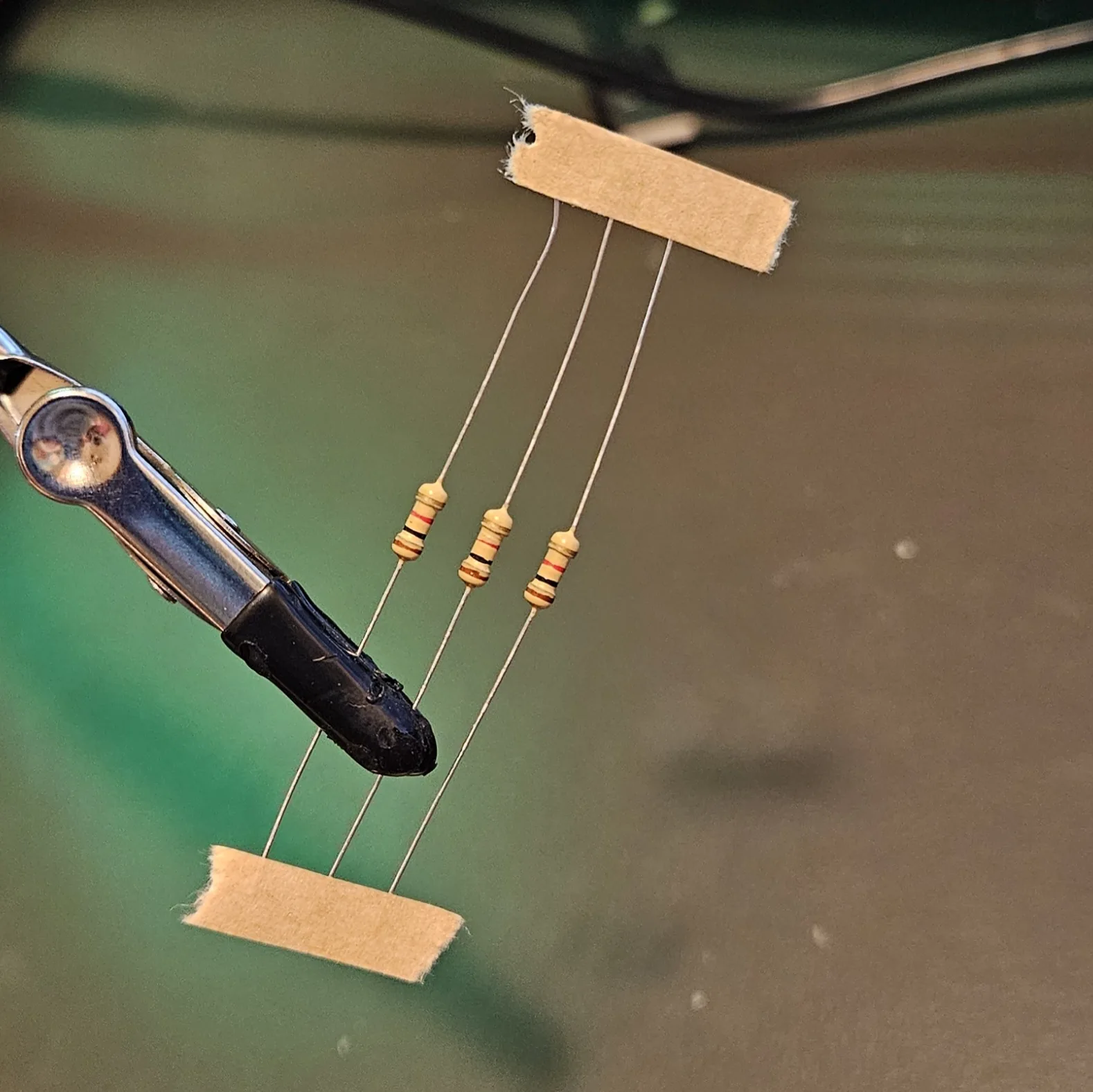 Three color-banded resistors suspended between two strips of tape, their long leads running top to bottom.