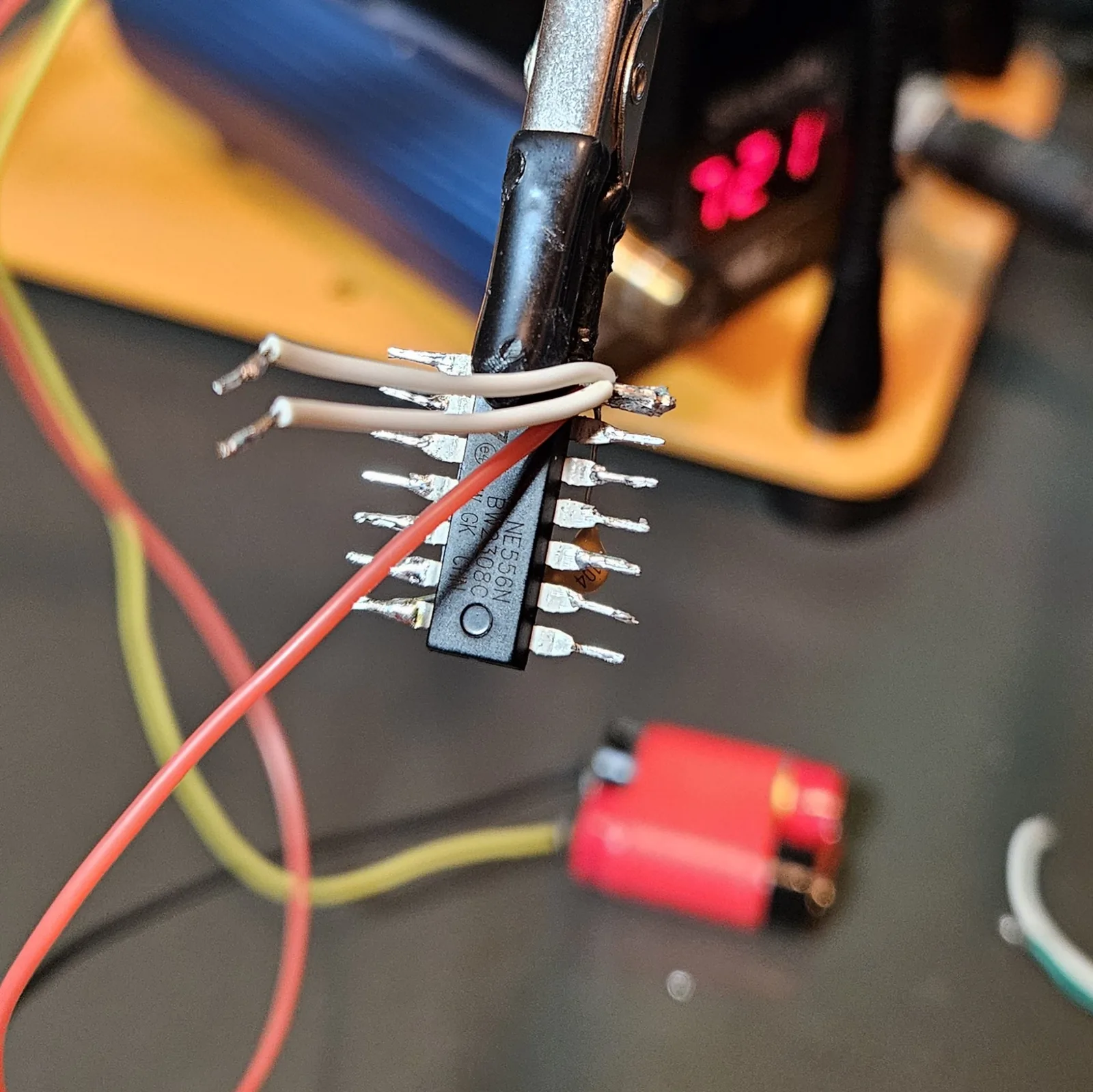 Two white insulated reset jumpers resting loose across the NE556's pins, the red V-plus supply lead crossing the chip behind them, everything dry-fit and nothing soldered yet.