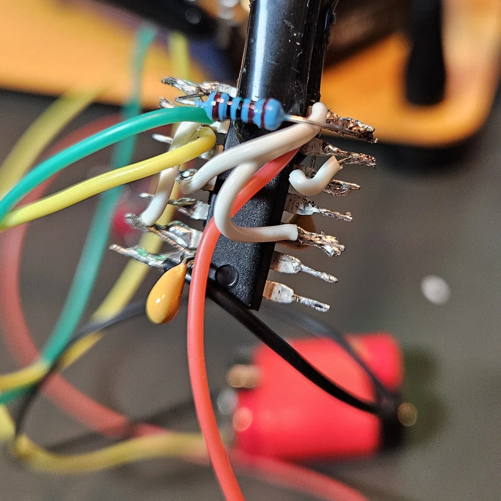 Close-up of timer A finished: the yellow timing cap, the blue 1K resistor, the white jumpers, and the pot leads all soldered point-to-point on the splayed chip.