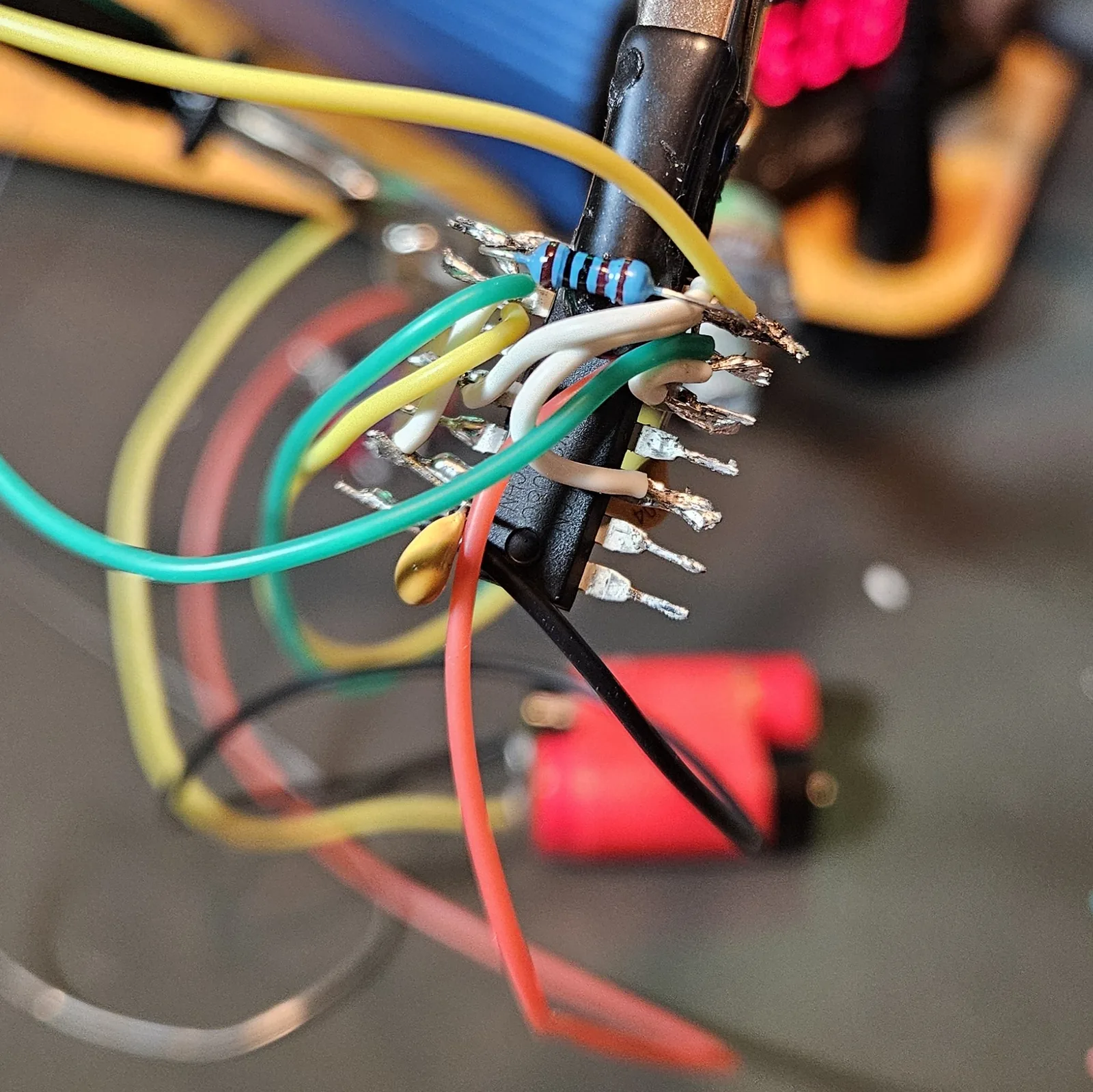 Dense point-to-point wiring building up on the chip: green and yellow pot leads, white jumpers, the red V-plus lead, the blue 1K resistor, and a yellow timing cap all converging on the pins.