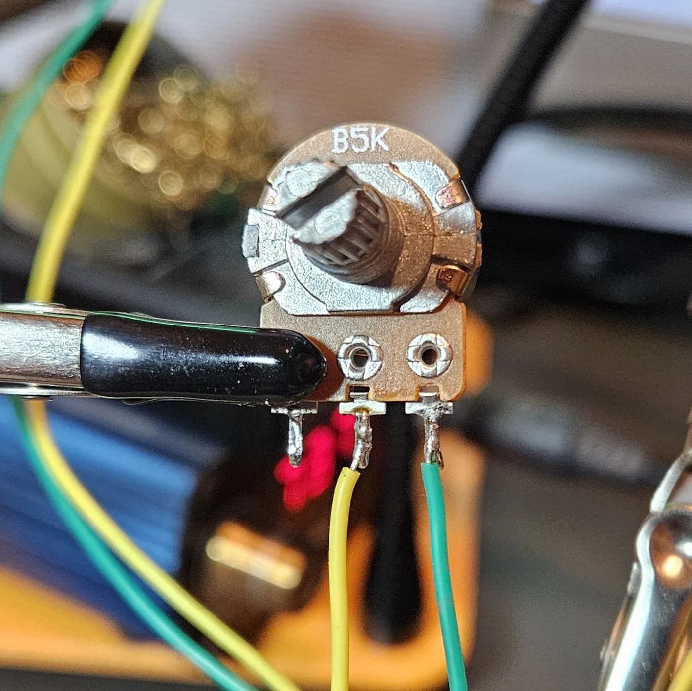 Front view of the wired B5K volume potentiometer showing its three solder lugs with the yellow and green leads attached.