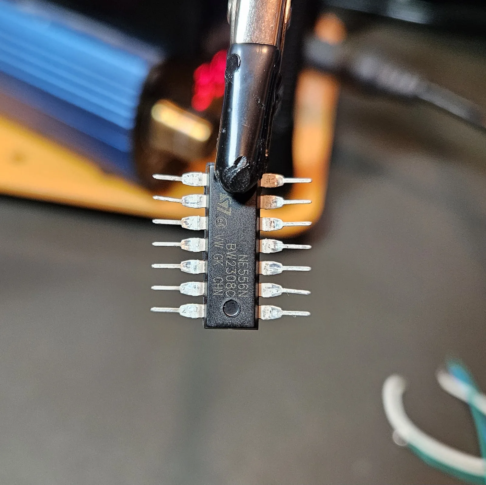 The splayed NE556 gripped in the helping-hands alligator clip, belly and pin-1 dimple facing outward, ready to be tinned.