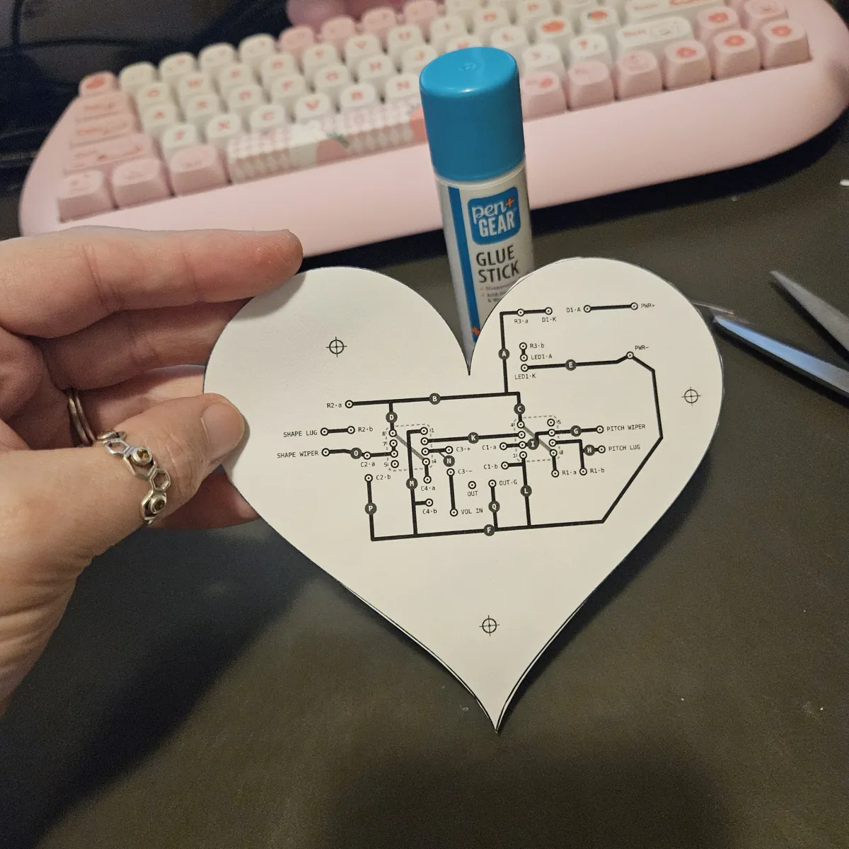 A hand holding the finished heart showing its BACK: bold black traces, ringed pads and the three pink targets, its outline lined up with the front all the way around.