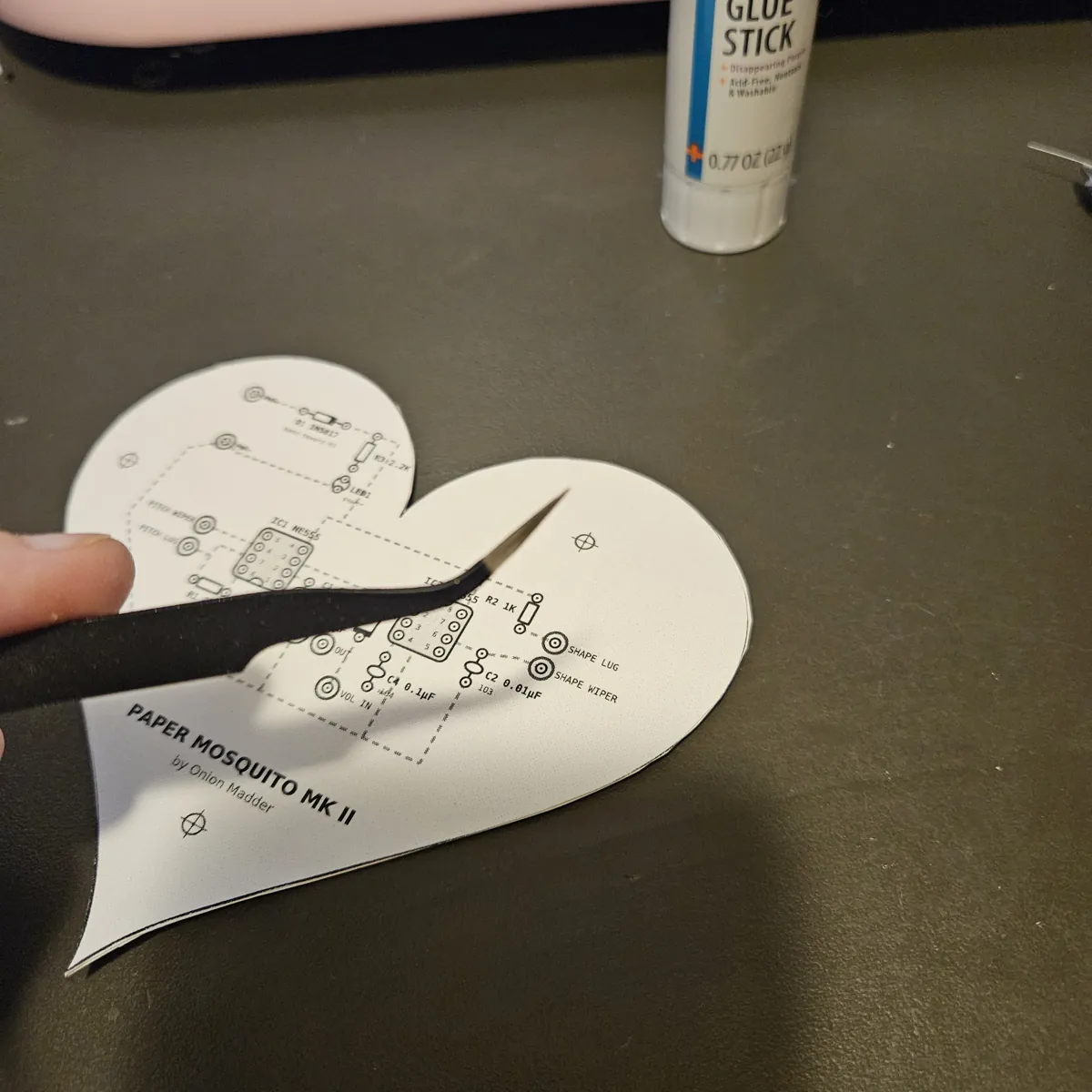 A pair of black pointed tweezers held over the front of the heart, aimed at the chip holes.
