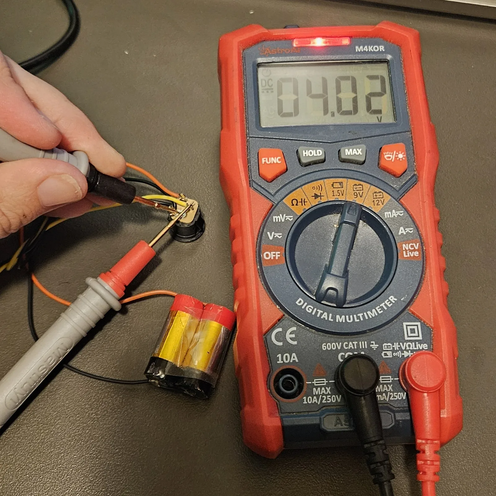 Testing the pack with a red digital multimeter - the screen reads 4.02 volts.