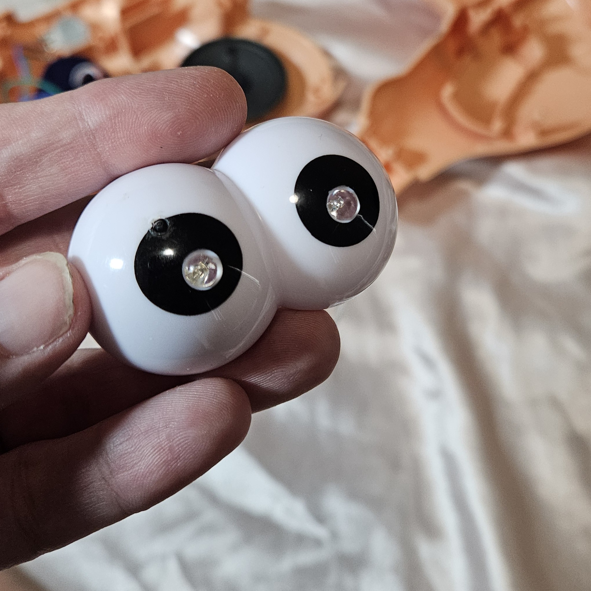 Close-up of the two eyeballs in hand, clear LED domes seated in the black pupils — one eye has an extra small hole drilled just off-center.