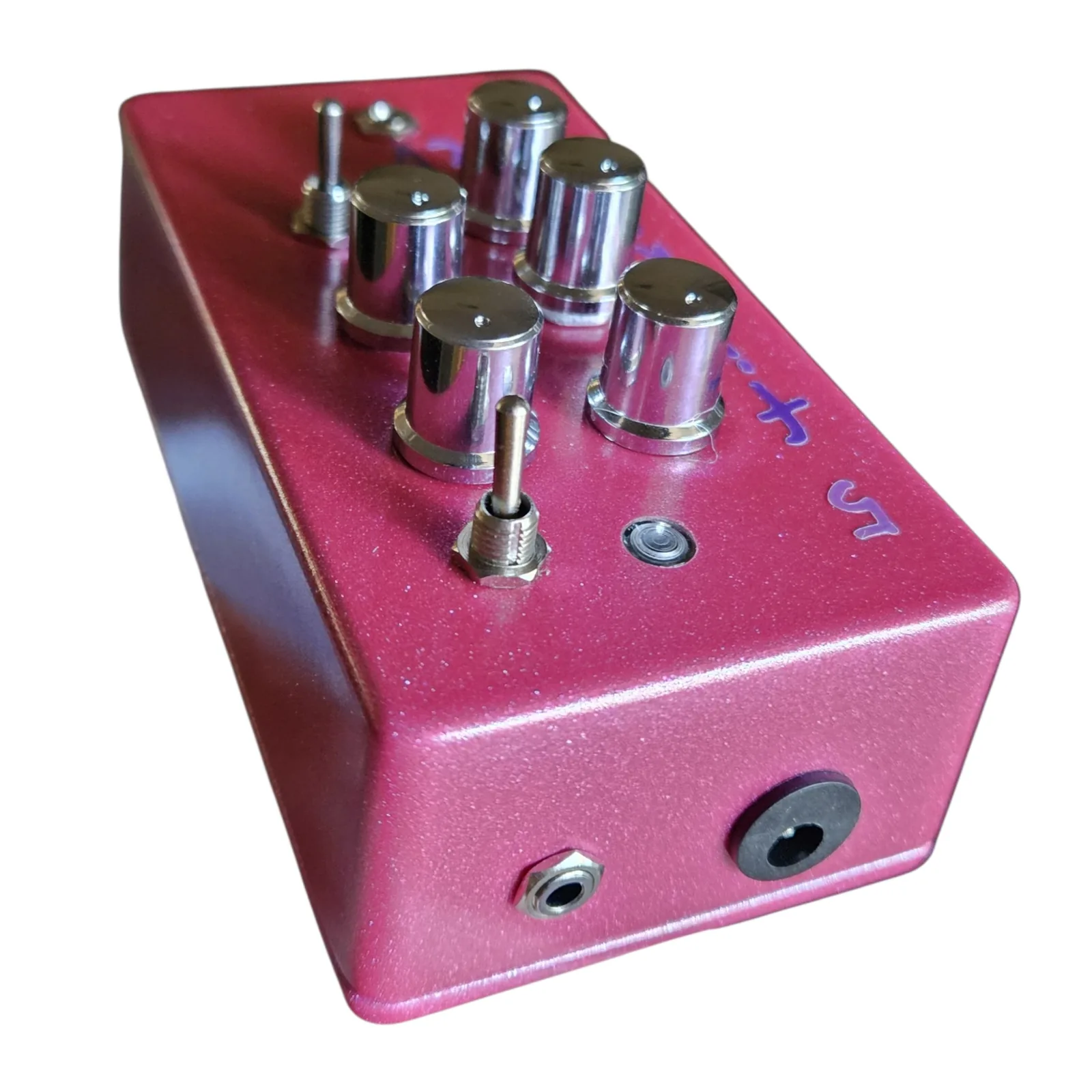 The pink box from above its top end, showing the edge with a small jack and a larger jack in it, and the five chrome knobs and the toggles standing up from the face beyond.