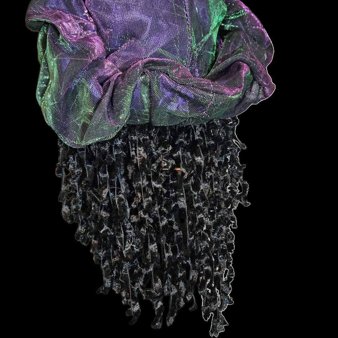Back of the head against black — no face visible. The iridescent purple-and-green cap gathers over the crown, and the black crushed-velvet ringlets hang below it in long ragged strands.