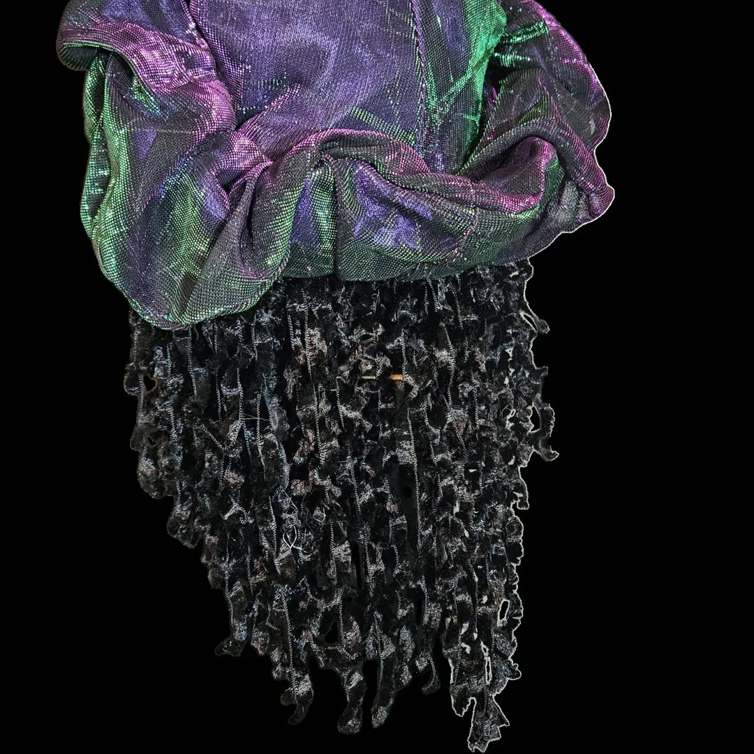 Back of the head against black - no face visible. The iridescent purple-and-green cap gathers over the crown, and the black crushed-velvet ringlets hang below it in long ragged strands.