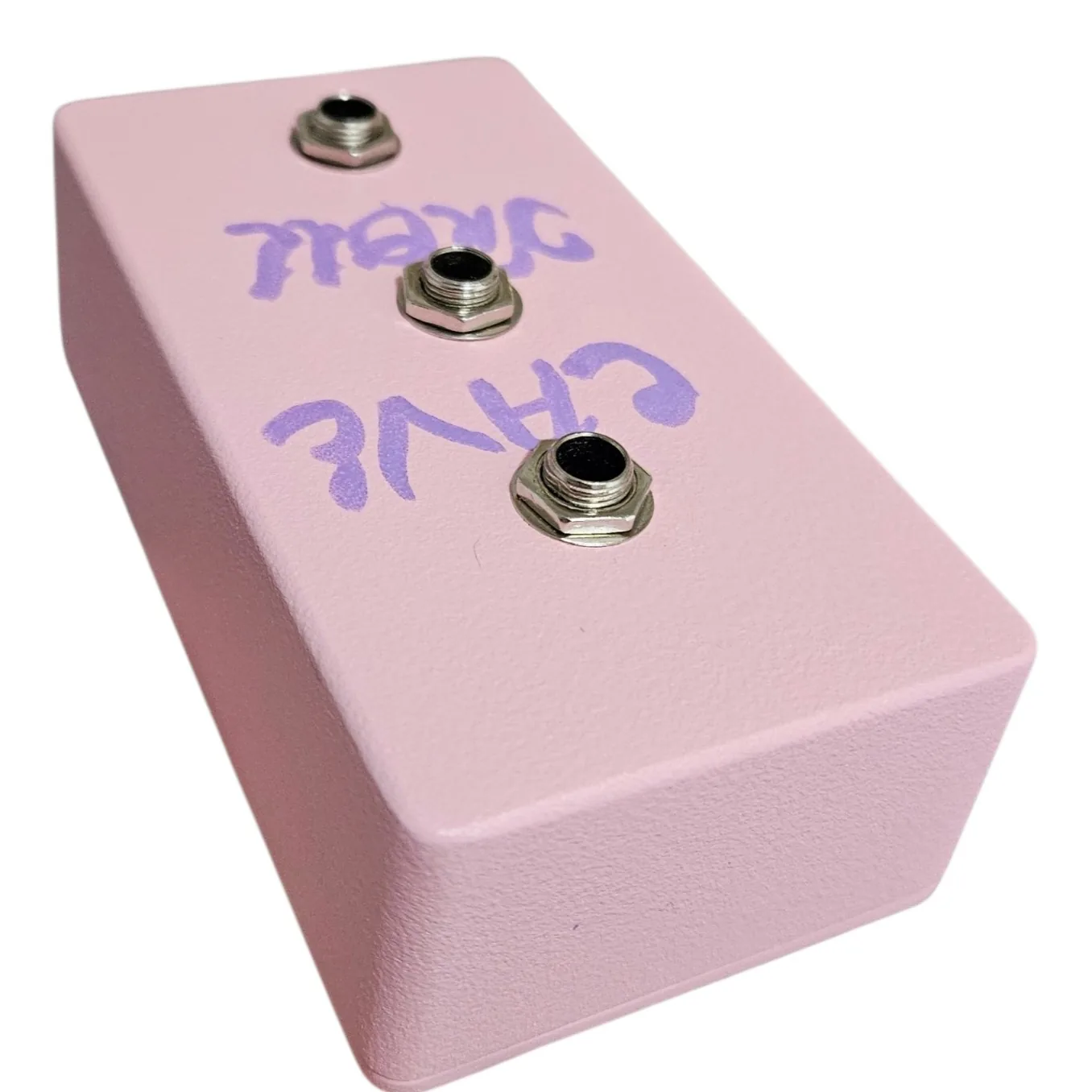 The pink box seen from above and turned over, so its depth and the top edge fill the frame and the lettering reads upside down. The three jack sockets run down the face and the rest of the enclosure is bare pink.