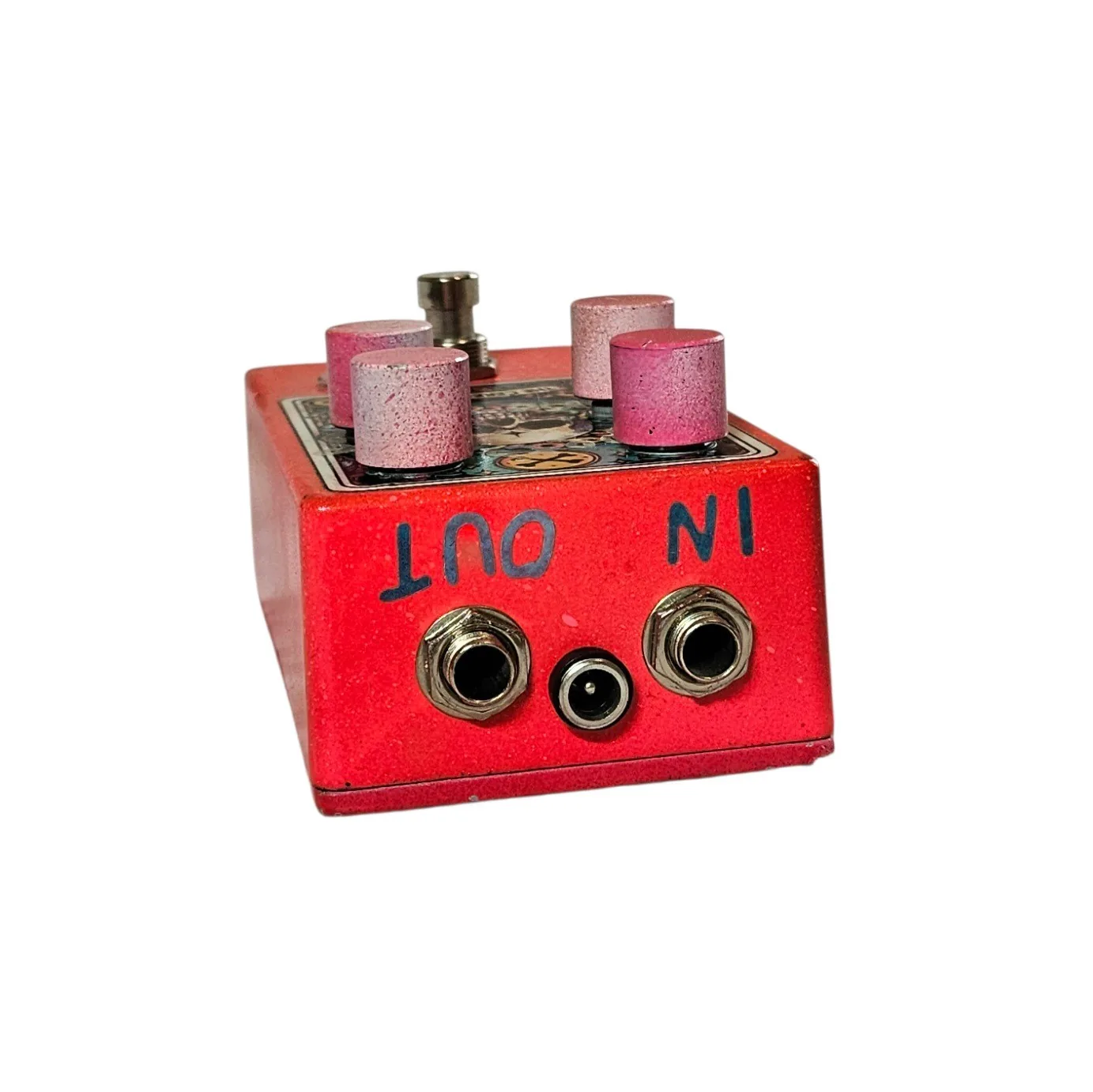 The top edge of the pedal, with IN and OUT written by hand in black marker beside a quarter-inch jack socket at each end and a barrel DC power socket centered between them.