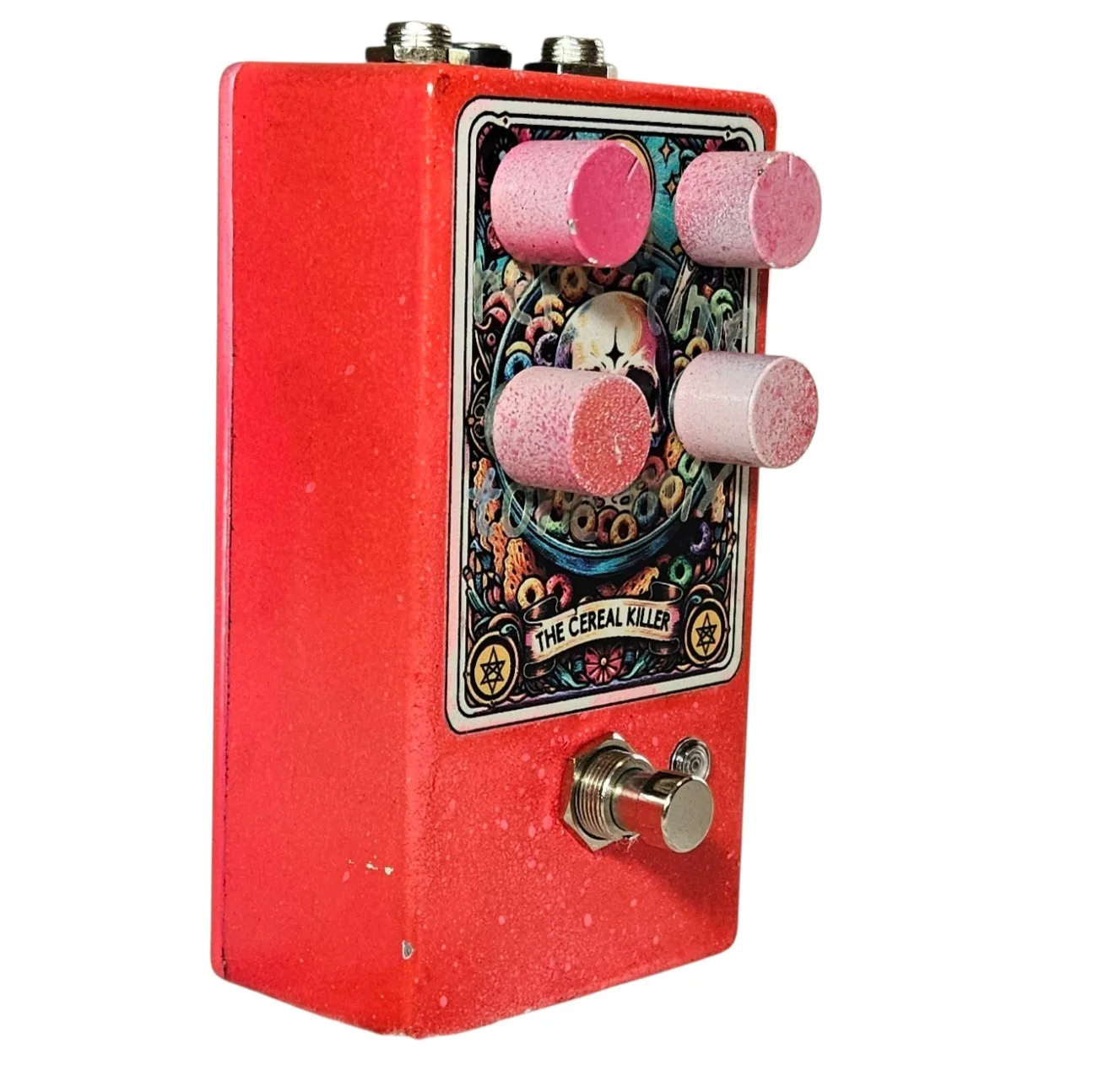 The pedal turned three quarters to show its depth: the red speckled flank runs back from the tarot-card face and the four dusty pink knobs stand well proud of it in profile. The footswitch projects from the lower front and jack sockets show along the top edge.