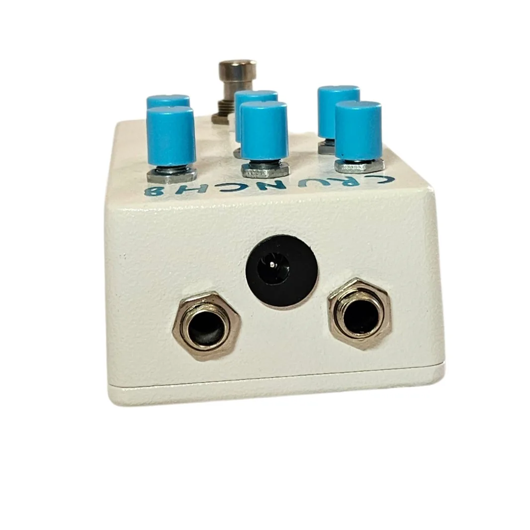 The top edge of the pedal straight on, with a silver quarter-inch jack socket at each end and a black barrel power socket centered between them. The blue knobs stand above and the CRUNCH8 lettering reads upside down from this angle.