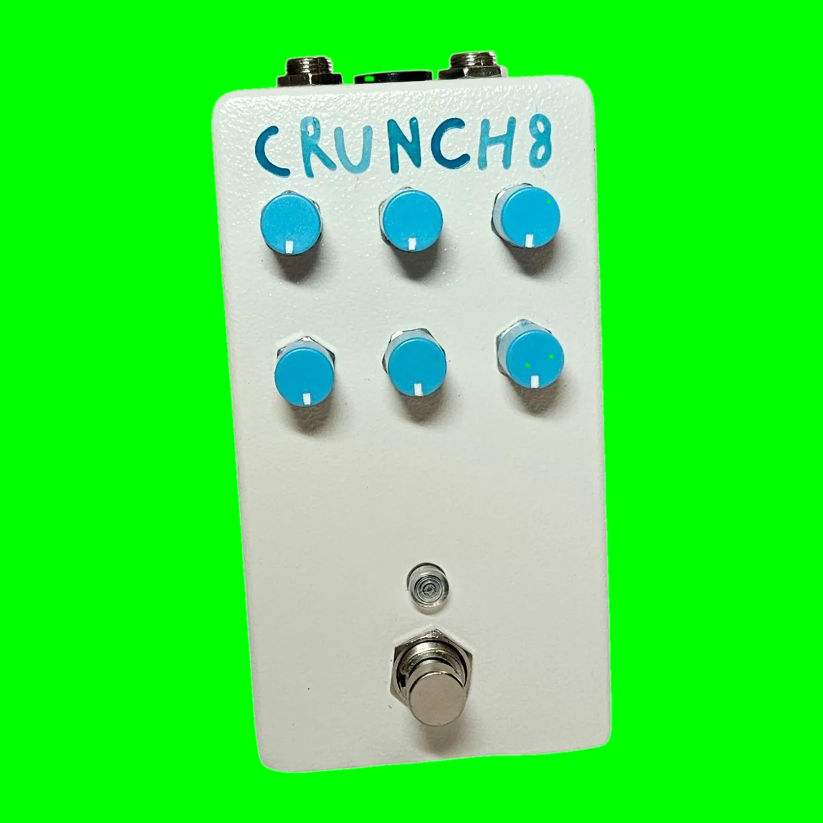 A white pedal with a lightly textured finish, photographed face on, with CRUNCH8 hand-painted across the top in bright blue capitals. Six sky-blue knobs stand in two rows of three below the lettering, a small LED sits under them, and a silver footswitch is at the bottom.