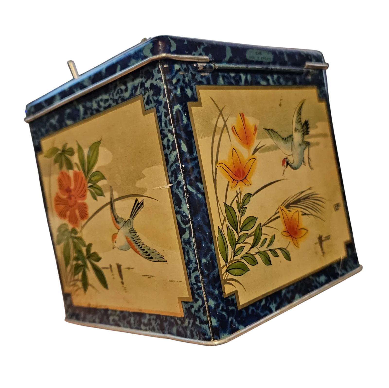 The tin from the side, showing two more painted panels - orange lilies and a long-tailed bird on each - inside the same mottled blue border. A single toggle lever stands up above the top edge.