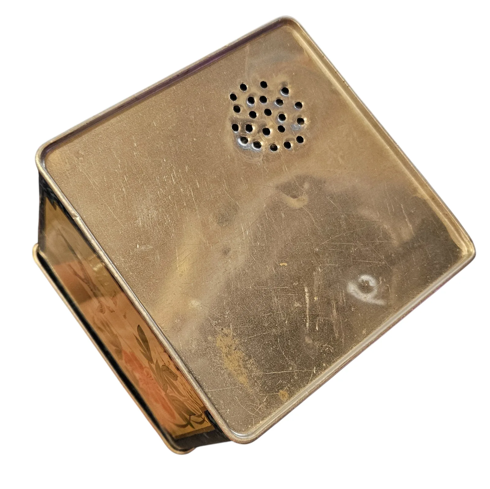 The bare underside of the tin: plain unpainted metal, lightly scuffed, with the decorated sides just visible around the edges.
