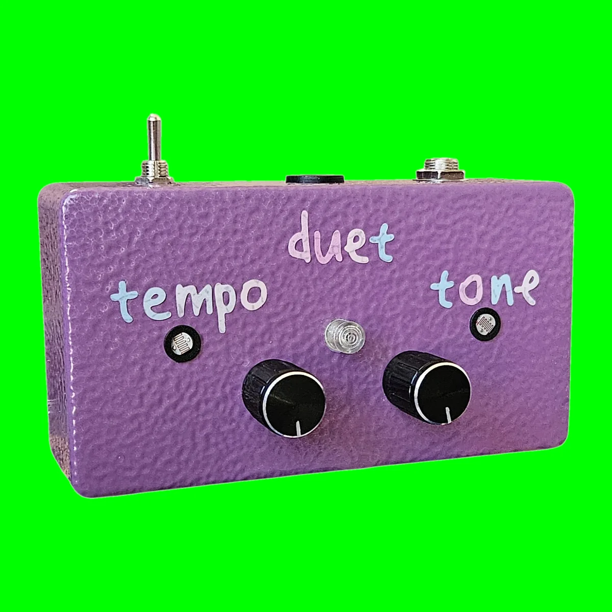 Duet - a purple hammertone box lying flat, duet lettered at the top with tempo and tone beside two small photocells, a clear LED dome in the middle, two black knobs below, and a toggle, a quarter-inch jack and a DC socket along the top edge