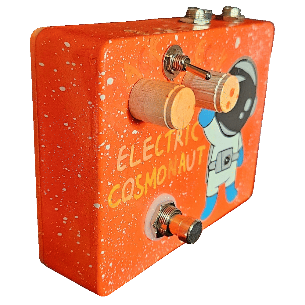 Left side of the pedal: an orange wall flecked with white speckle, showing the two cream knobs and the toggle switch standing out from the face and the footswitch protruding at the bottom. Hand-lettered "ELECTRIC COSMONAUT" runs across the front in cream and yellow beside the waving astronaut.