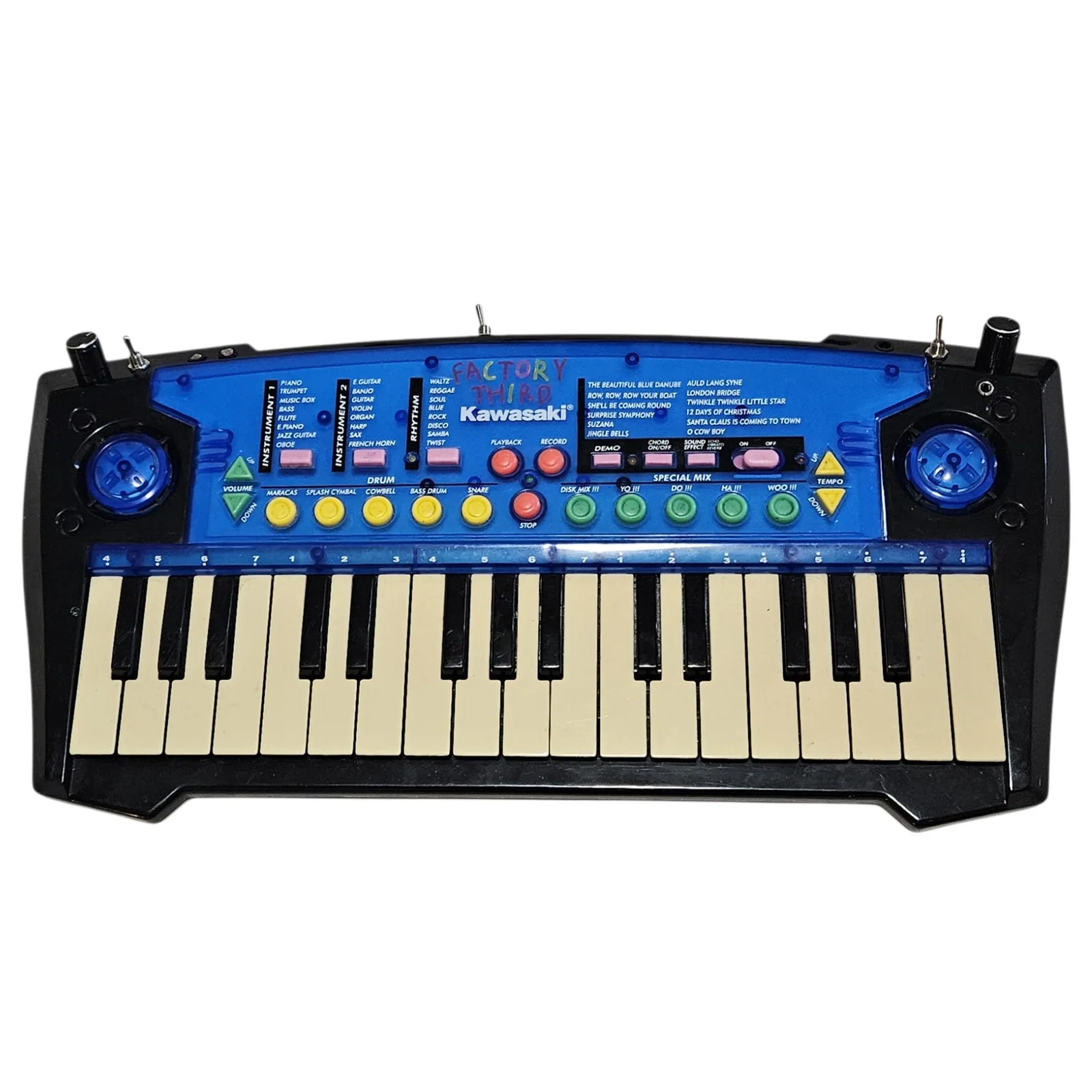 The keyboard head on against white: a black case with a bright blue control panel and 32 keys, the white ones yellowed with age. FACTORY THIRD is hand-lettered across the panel above the Kawasaki logo in red, pink, blue and green marker. Around it the original 1990s toy graphics are untouched - printed lists headed INSTRUMENT 1, INSTRUMENT 2 and RHYTHM, a column of demo song titles, five yellow drum buttons, three red transport buttons and five green SPECIAL MIX buttons. A round blue speaker grille sits at each end, and added along the top edge are two black knobs at the outer corners and three silver toggle switches.