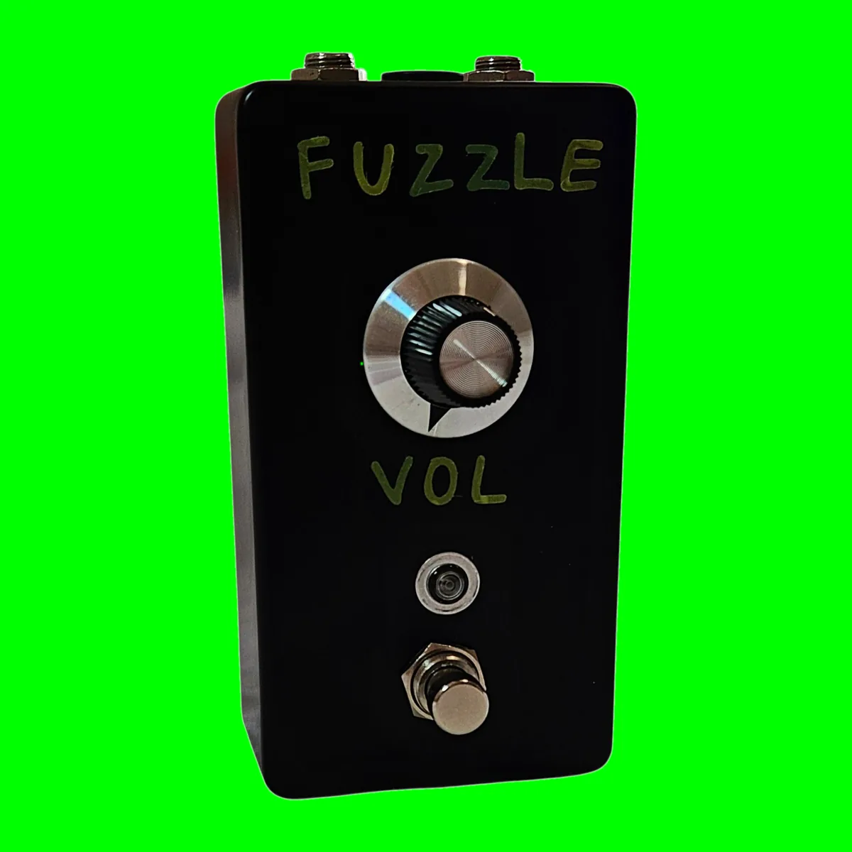 A tall black pedal photographed face on. Hand-painted green capital letters spell FUZZLE across the top and VOL below the knob. A single large knob with a silver collar and a pointer line sits in the middle, a small round LED below it, and a silver footswitch at the bottom.