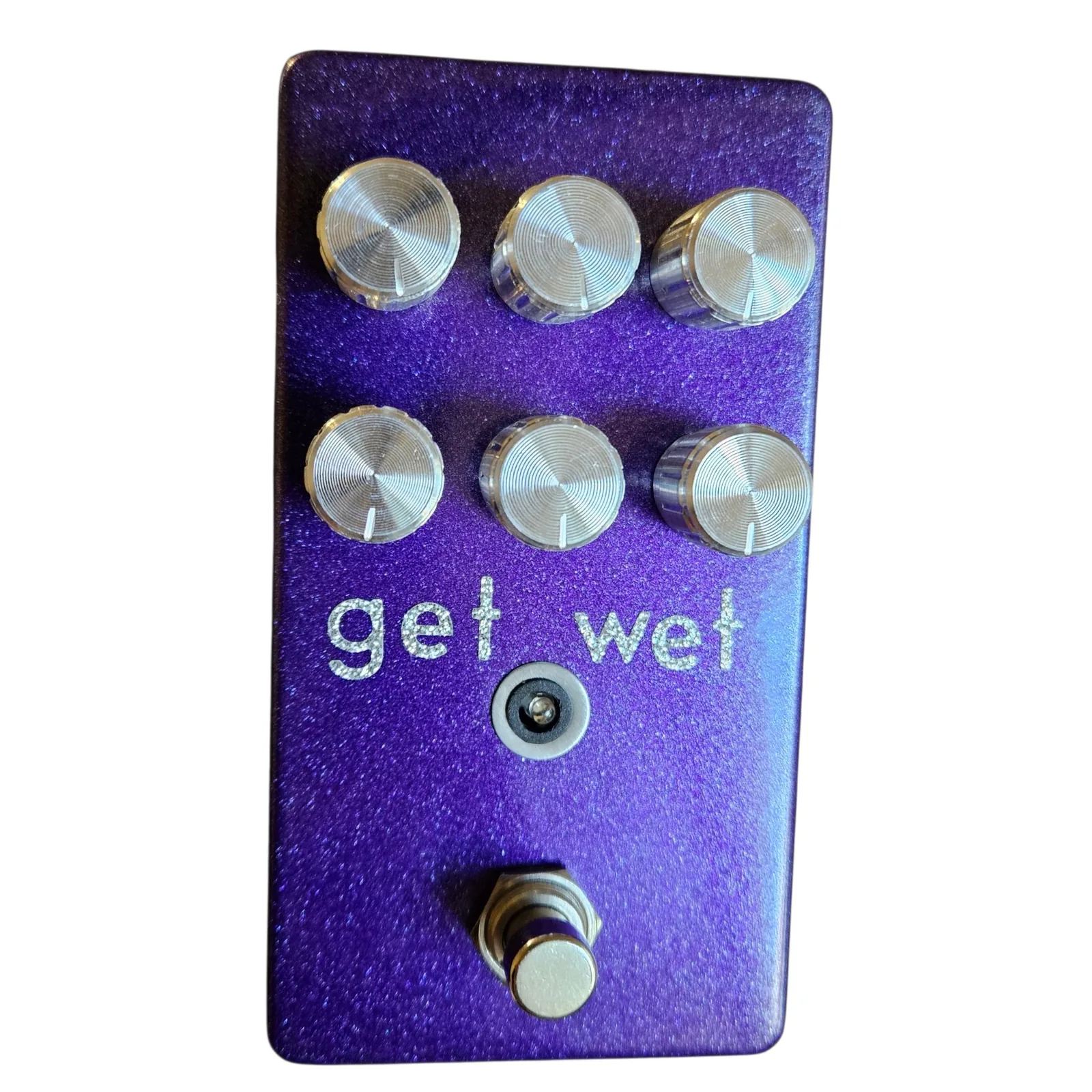 Get Wet pedal, front view - a tall metallic purple glitter enclosure with six chrome knobs in two rows of three, get wet hand-lettered in sparkly silver below them, a small LED under the lettering, and a silver footswitch at the bottom.