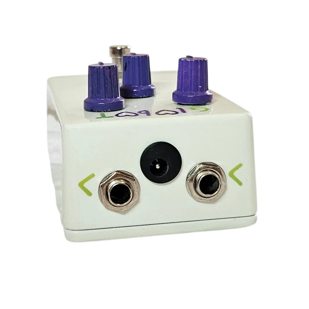 The top edge of the pedal straight on, with a silver quarter-inch jack socket at each end and a black barrel power socket centered between them. The input is at the left and the output at the right. A small hand-painted green arrow sits beside each jack marking the signal direction, and the lettering reads upside down from here.