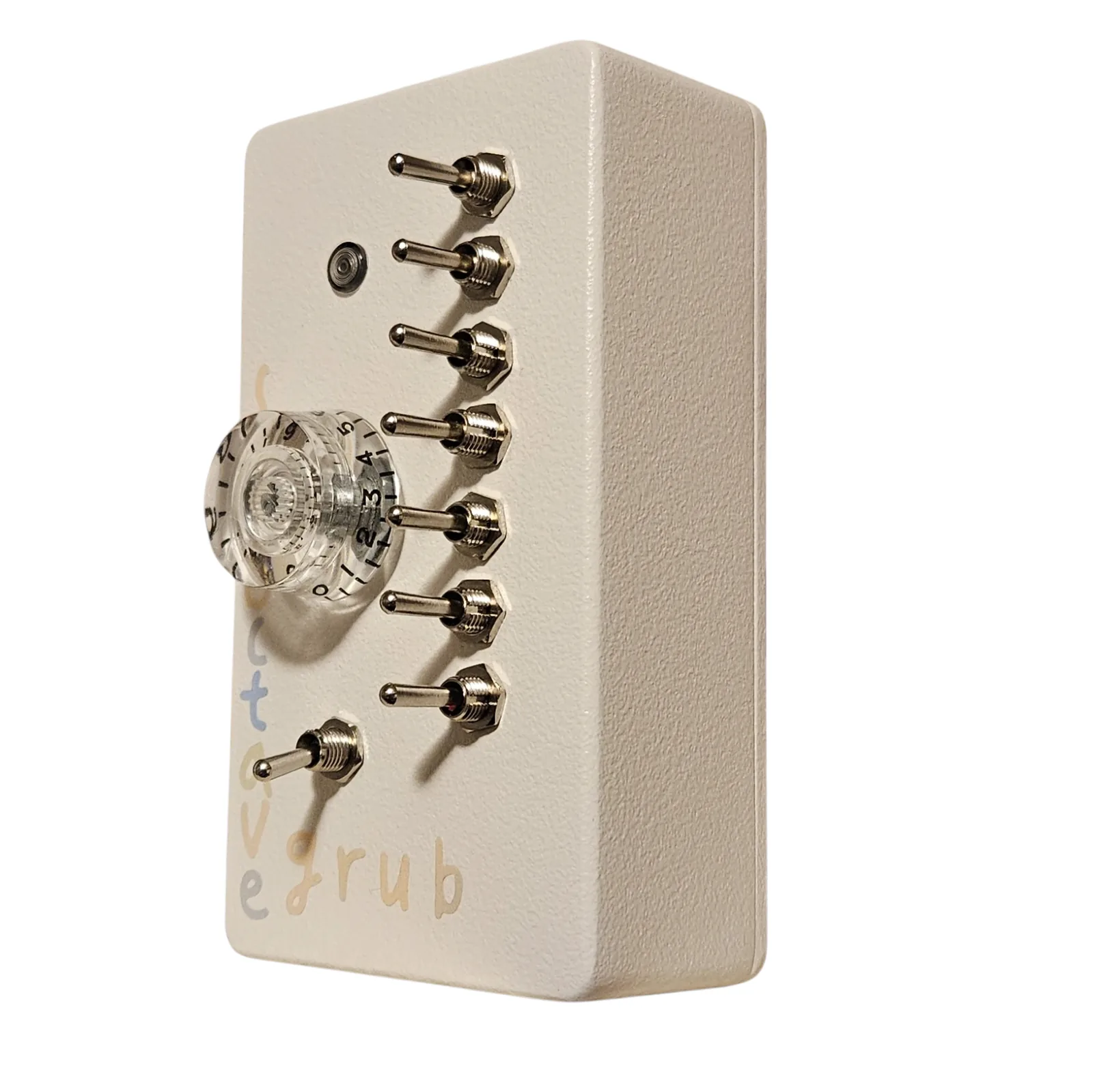 The box turned the other way, showing the depth of the off-white enclosure and its long side wall. The seven toggles and the eighth below them stand out in silhouette, the clear numbered knob sits at the left of the face, and the pastel lettering runs down the far edge.