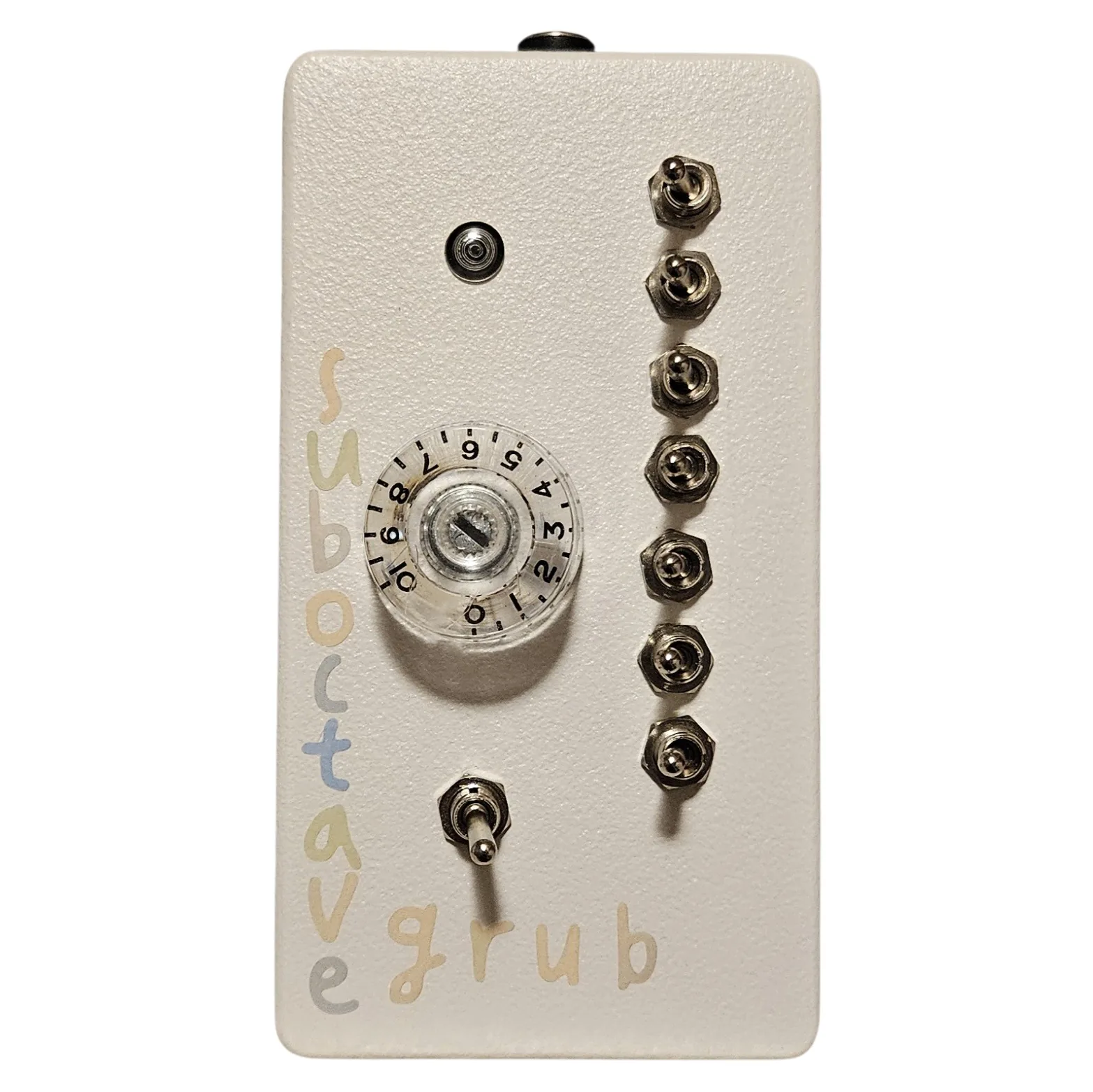 An upright off-white box photographed face on. A small LED sits near the top and a clear plastic knob with a numbered dial skirt reading zero to ten sits in the middle. Seven chrome toggle switches run down the right-hand side in a gentle arc and an eighth sits at the bottom center. The words sub octave run down the left edge in pastel cream, blue and gray hand lettering, with grub across the bottom in cream. A black jack is just visible on the top edge.