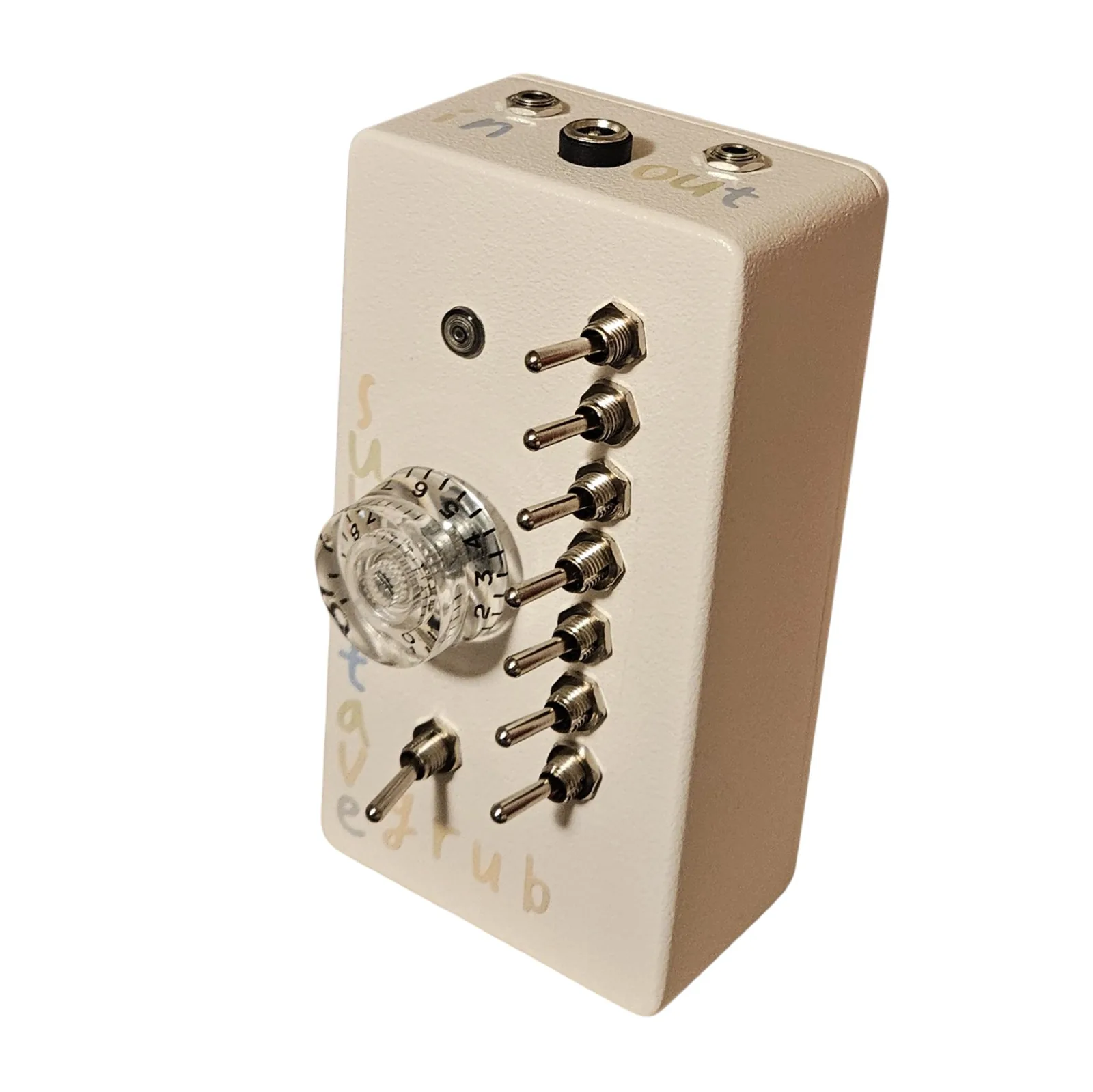 The box from above and in front, showing the top edge. Three sockets sit along it: a small silver jack lettered in, a black barrel DC socket in the middle, and a second silver jack lettered out, the words hand-lettered in pale blue. Below, the face falls away with the LED, the numbered knob, the row of toggles and the sub octave grub lettering.