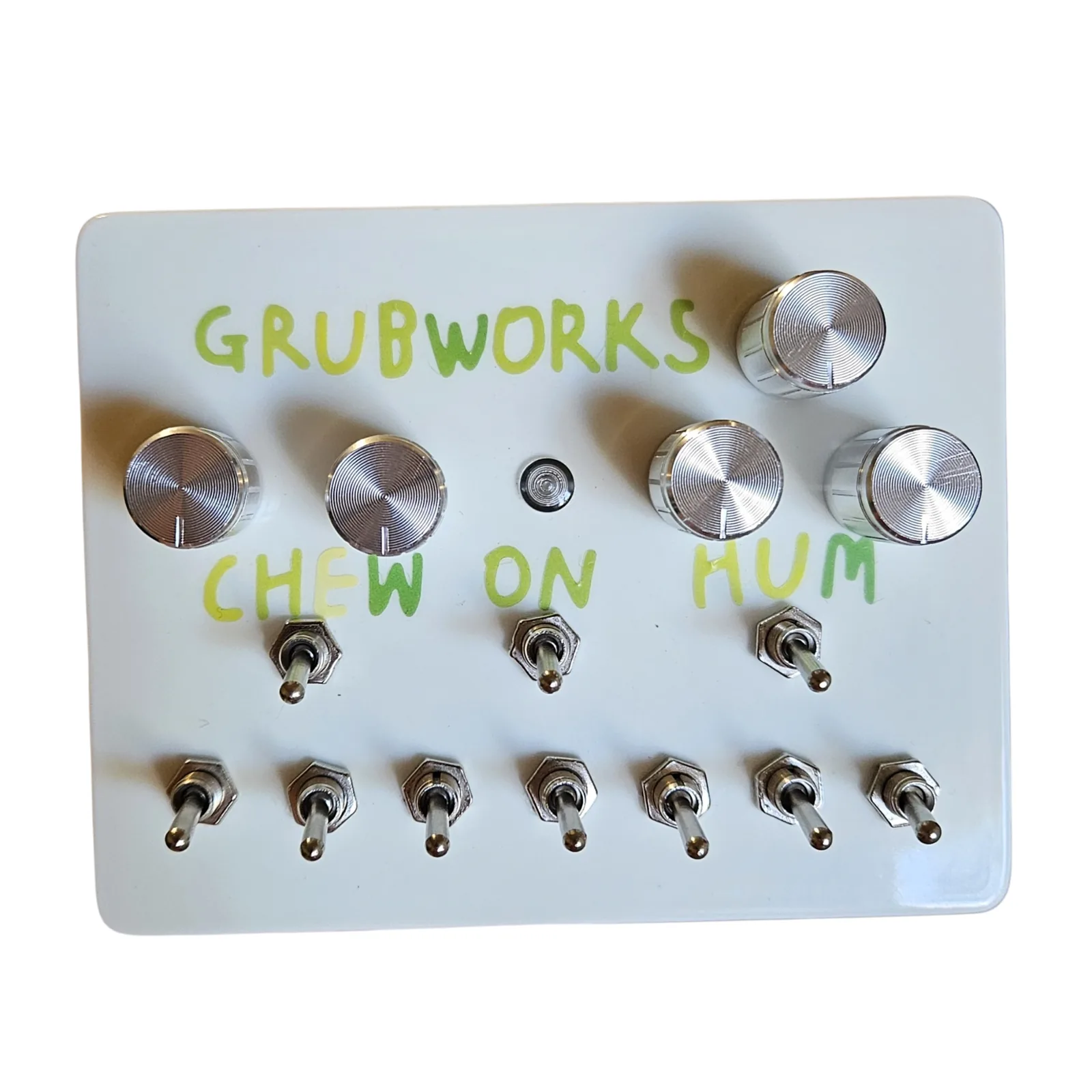 A glossy white box photographed face on, GRUBWORKS hand-lettered across the top in green, with a chrome knob on its own at the top right. Below the name is a row of four chrome knobs, two at the left and two at the right, with a small LED between them. CHEW, ON and HUM are lettered across the middle, each over a toggle, and a row of seven toggles runs along the bottom edge.