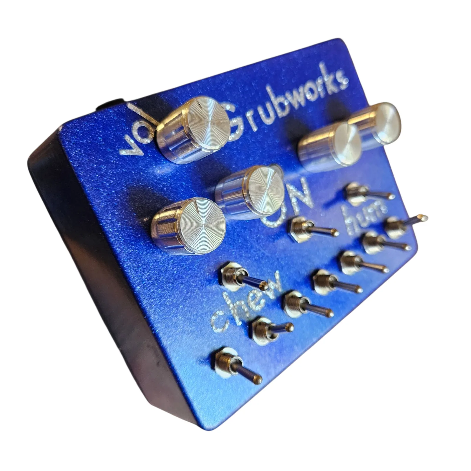 The box from the front left at a low angle, the chrome knobs standing tall in the foreground with vol and Grubworks lettered behind them, and the words ON, chew and hum among the toggles below.