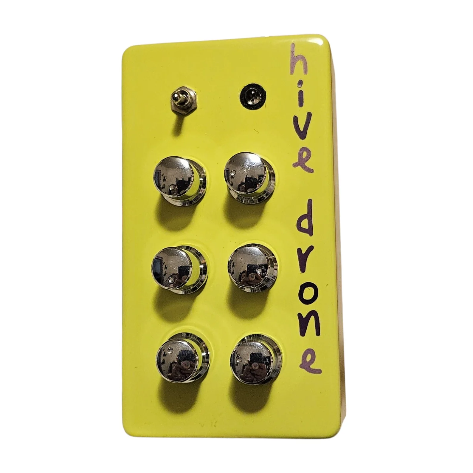 An upright neon green box photographed face on. A small chrome toggle switch sits at the top left and a black LED bezel at the top center. Below them six chrome knurled knobs stand in two columns of three, and the words hive drone run down the right side of the face in dark purple hand lettering.