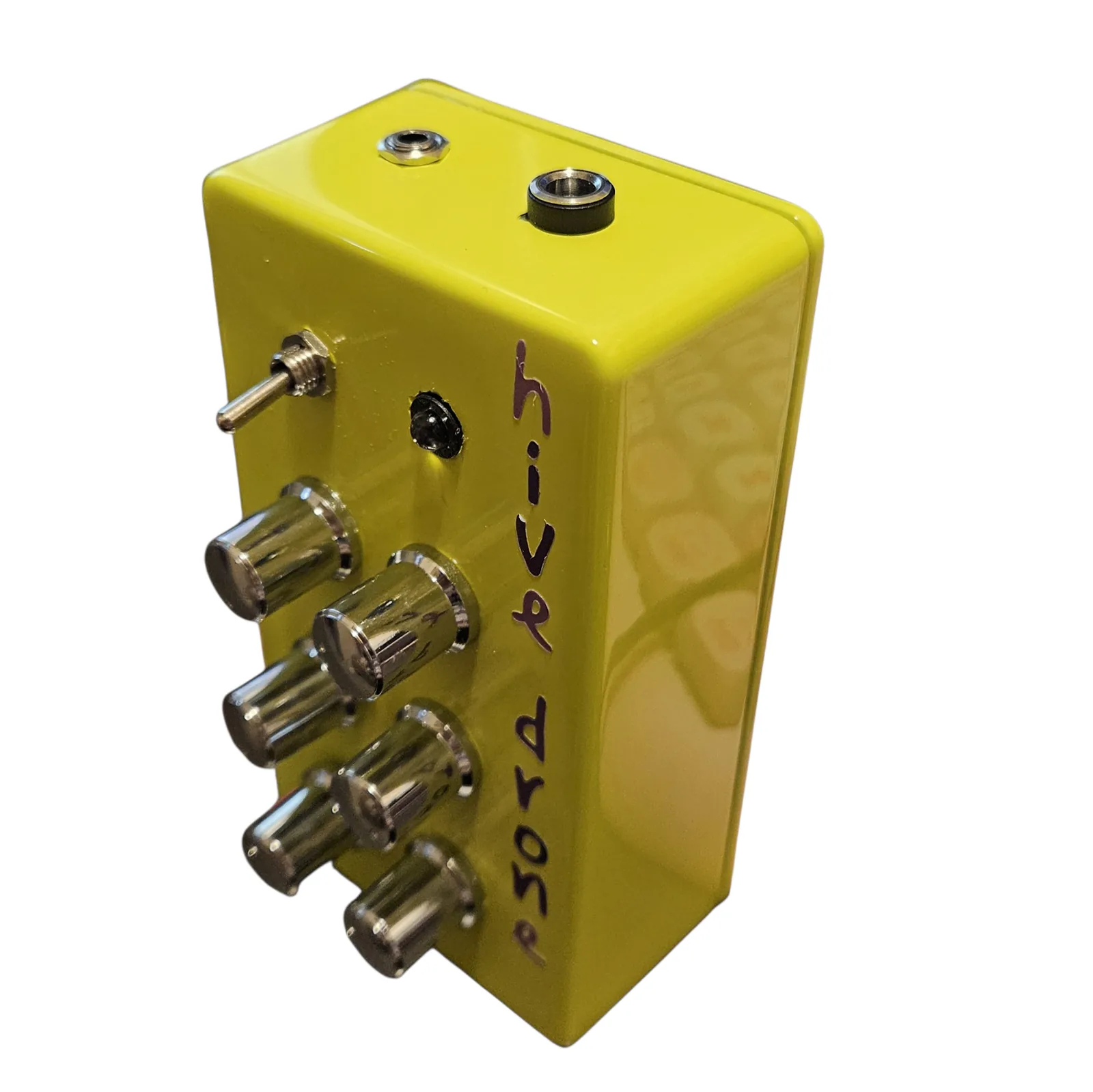 The box seen from above at an angle. On the top wall sit a small output jack and a black barrel DC socket, and below it the face falls away with the toggle, the LED bezel and the six chrome knobs.