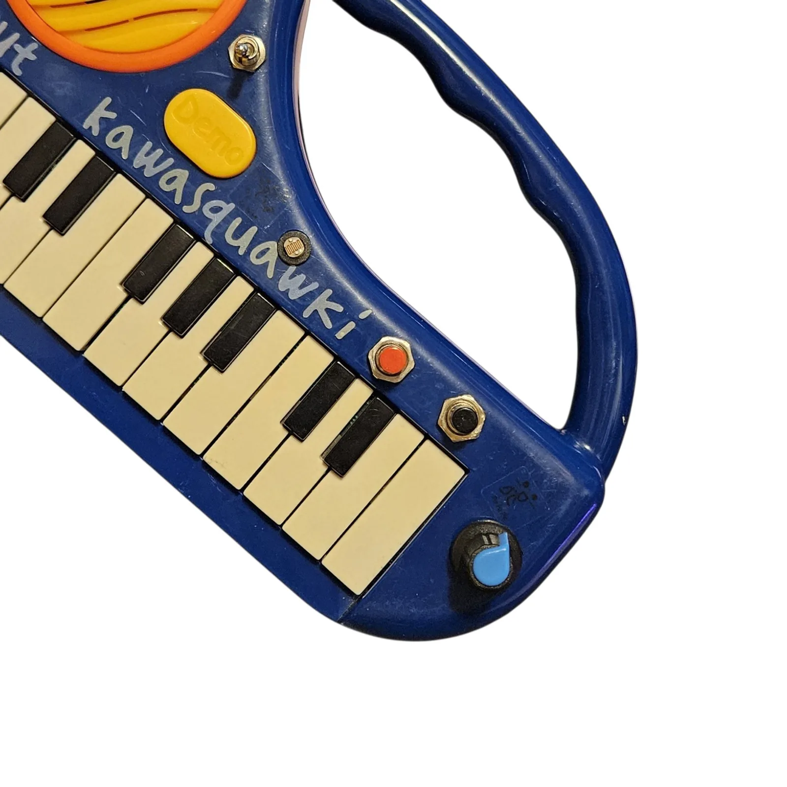 A close angled view of the right end of the panel. A red push button and a black push button sit in a row above the keys, with a small round photocell just above them and a black knob with a blue teardrop pointer at the bottom right corner. The hand-lettered kawasquawki runs across the middle and the yellow Demo button and orange speaker ring are at the top left.