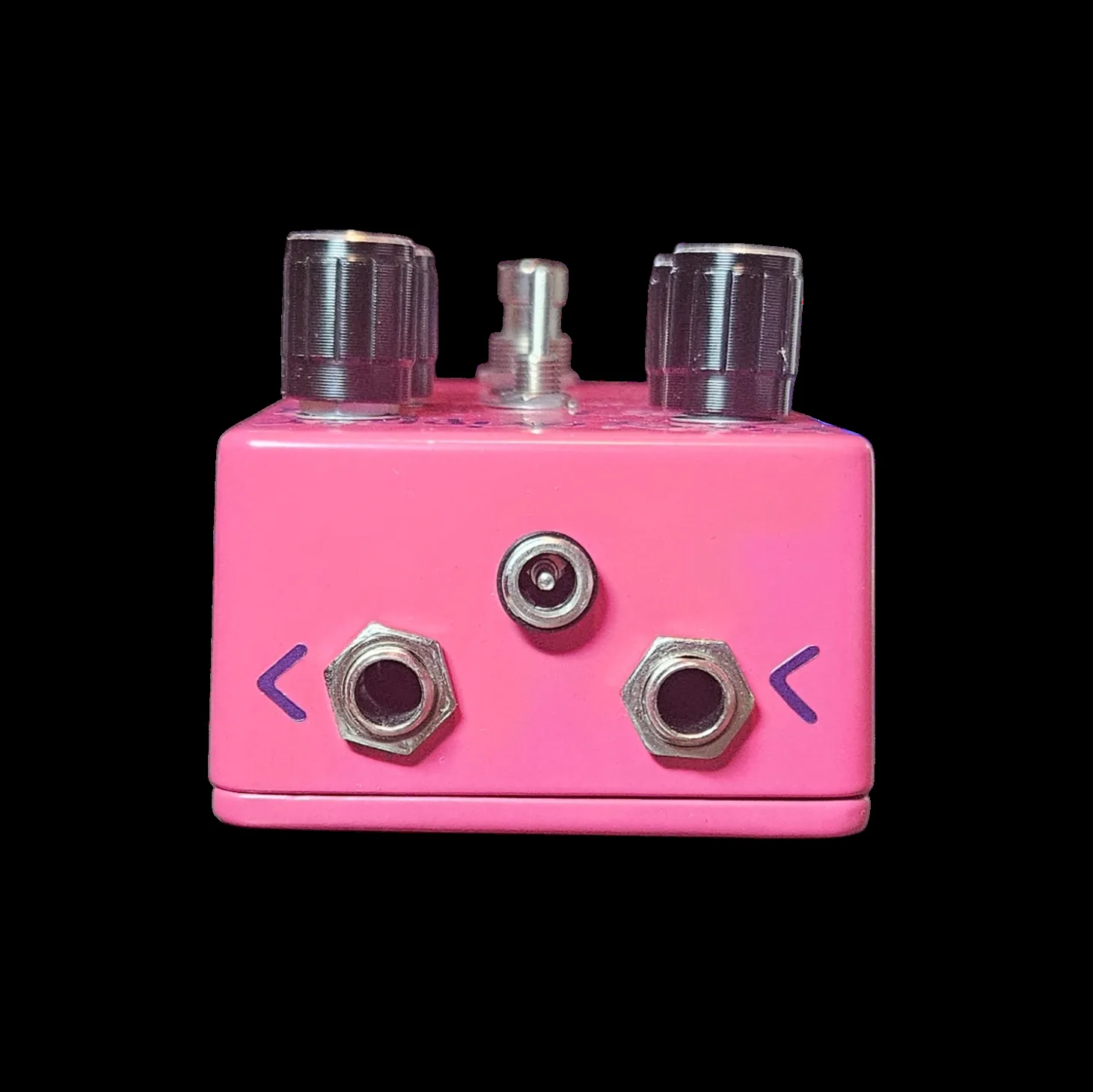 The top edge of the pedal photographed straight on. The input jack is at the left and the output at the right, with a barrel jack for the power supply between them, set higher. A small purple arrow is painted outboard of each of the two big jacks. The tops of two knobs and the toggle switch show along the upper edge of the frame.