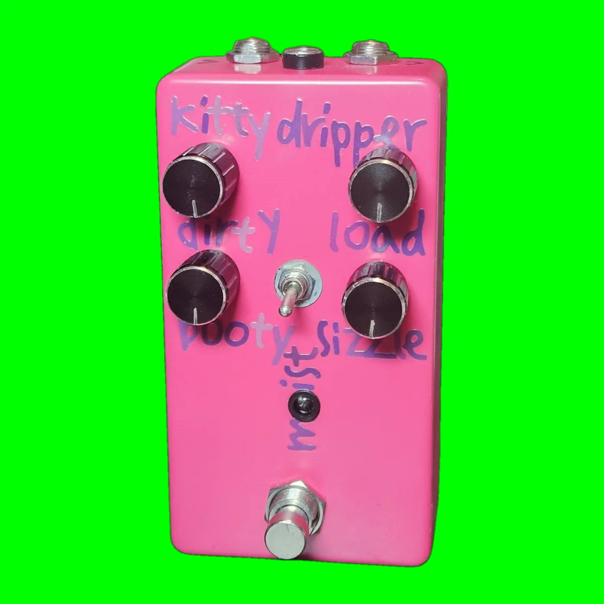 A hot pink pedal photographed face on. The words kitty dripper are hand-lettered across the top in purple marker. Four black knurled knobs sit in two rows, marked dirty and load along the top and booty and sizzle below. Between the lower two knobs is a small silver toggle switch with the word moist written up its side, and under that a black LED and a silver footswitch. Three jack nuts show along the top edge.