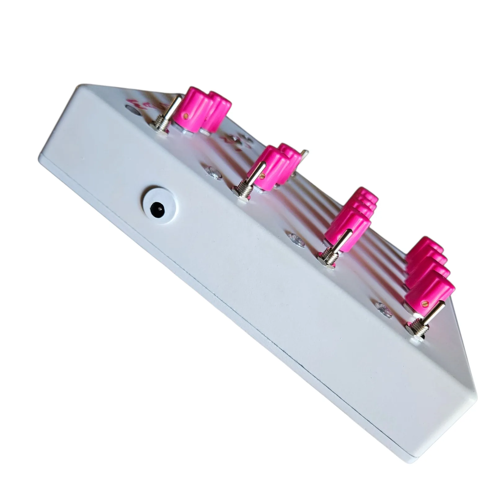The white box from its side, edge on, with a round barrel power jack in the side wall and the pink knobs and toggles standing up from the face in a row.