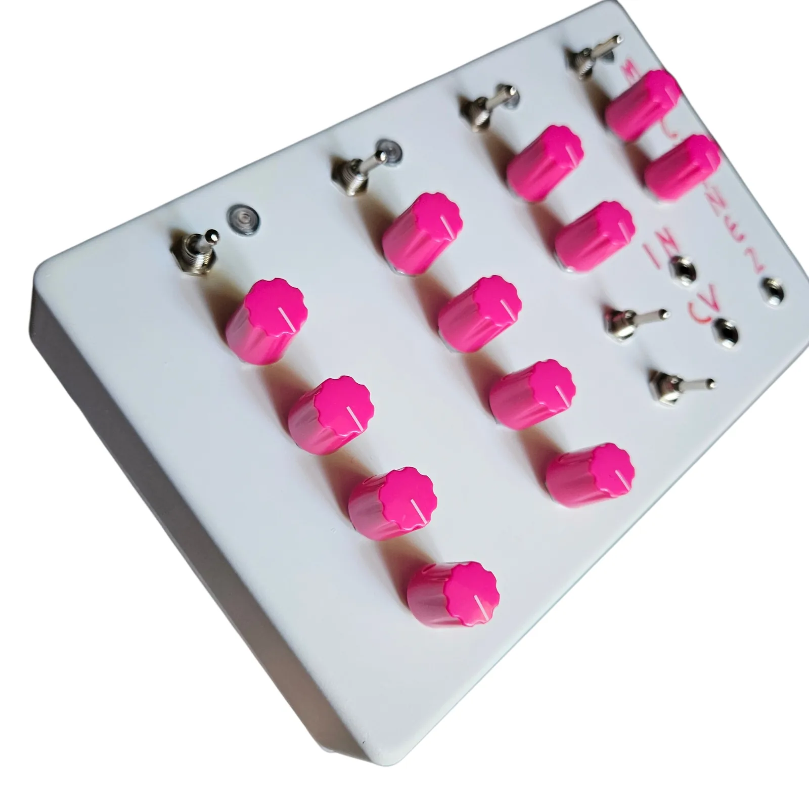 The white box at a steep angle from the left, the columns of pink knobs receding toward the lettered corner, the row of toggles and LEDs along the top edge.