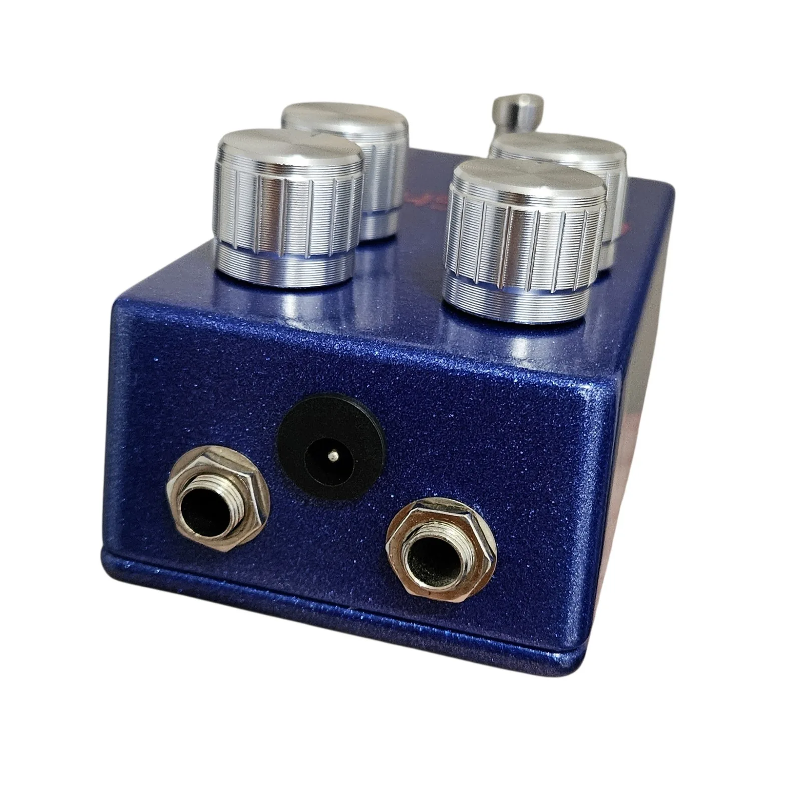 The top edge of the pedal, showing two quarter-inch jack sockets with silver nuts and a black DC barrel socket between them, with the four knobs standing above.