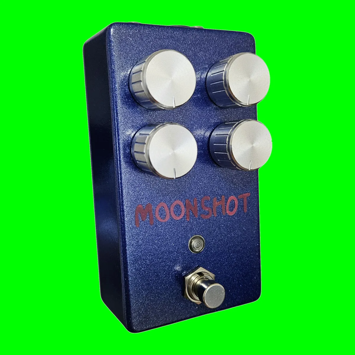 The Moonshot pedal stood upright and seen from the front left on white. A blue sparkle 125B enclosure with four silver knurled knobs in a two by two square, the word MOONSHOT hand-lettered across the face in red marker below them, a small indicator lens under the lettering and a silver footswitch at the bottom.
