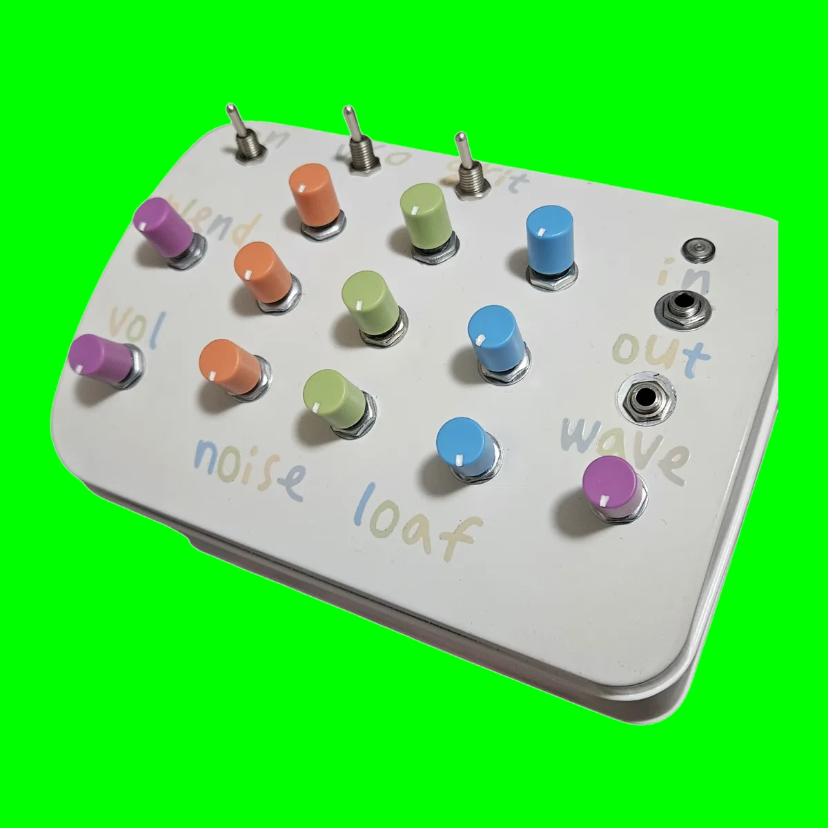 Noise Loaf - a white-painted loaf tin whose lid carries twelve small knobs in purple, orange, green and blue, three chrome toggles lettered on, vco and grit, an unlit LED and two small sockets lettered in and out, with noise loaf hand-lettered across the bottom, on a chroma green tile