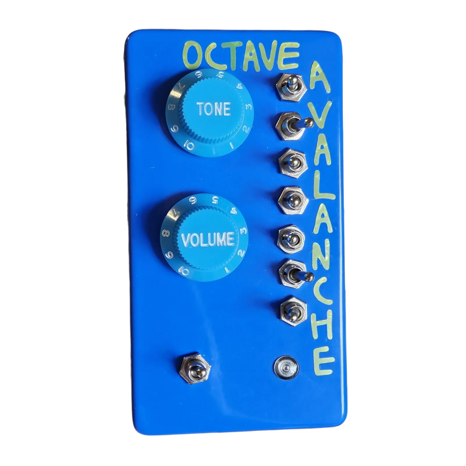 An upright glossy blue box photographed face on, OCTAVE hand-lettered in pale green across the top and AVALANCHE running down the right edge. Two light blue knobs with numbered skirts, lettered TONE and VOLUME, sit one above the other on the left, seven chrome toggle switches run down the right, and at the bottom there is a toggle on the left and a small round bezel on the right.